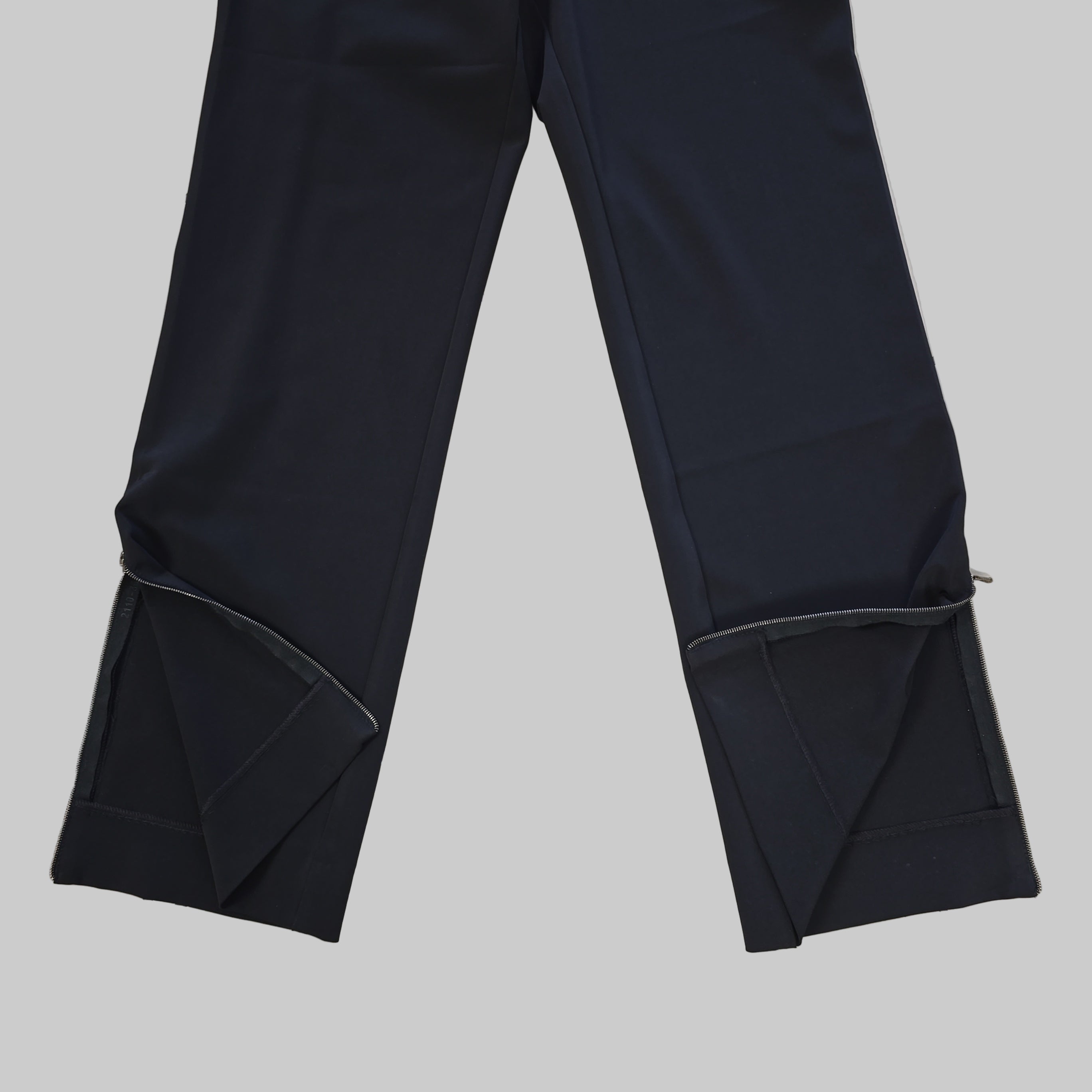 Two pairs of black pant legs laid flat on a tiled floor.