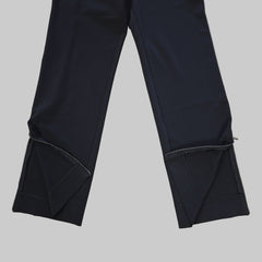 Two pairs of black pant legs laid flat on a tiled floor.