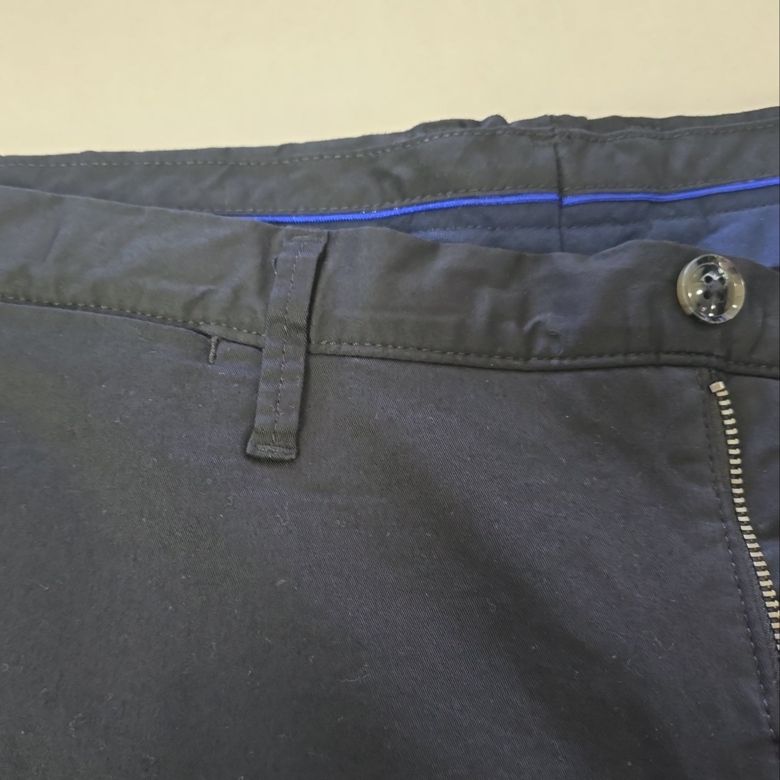 Close-up of black pants with a button and zipper on a beige background