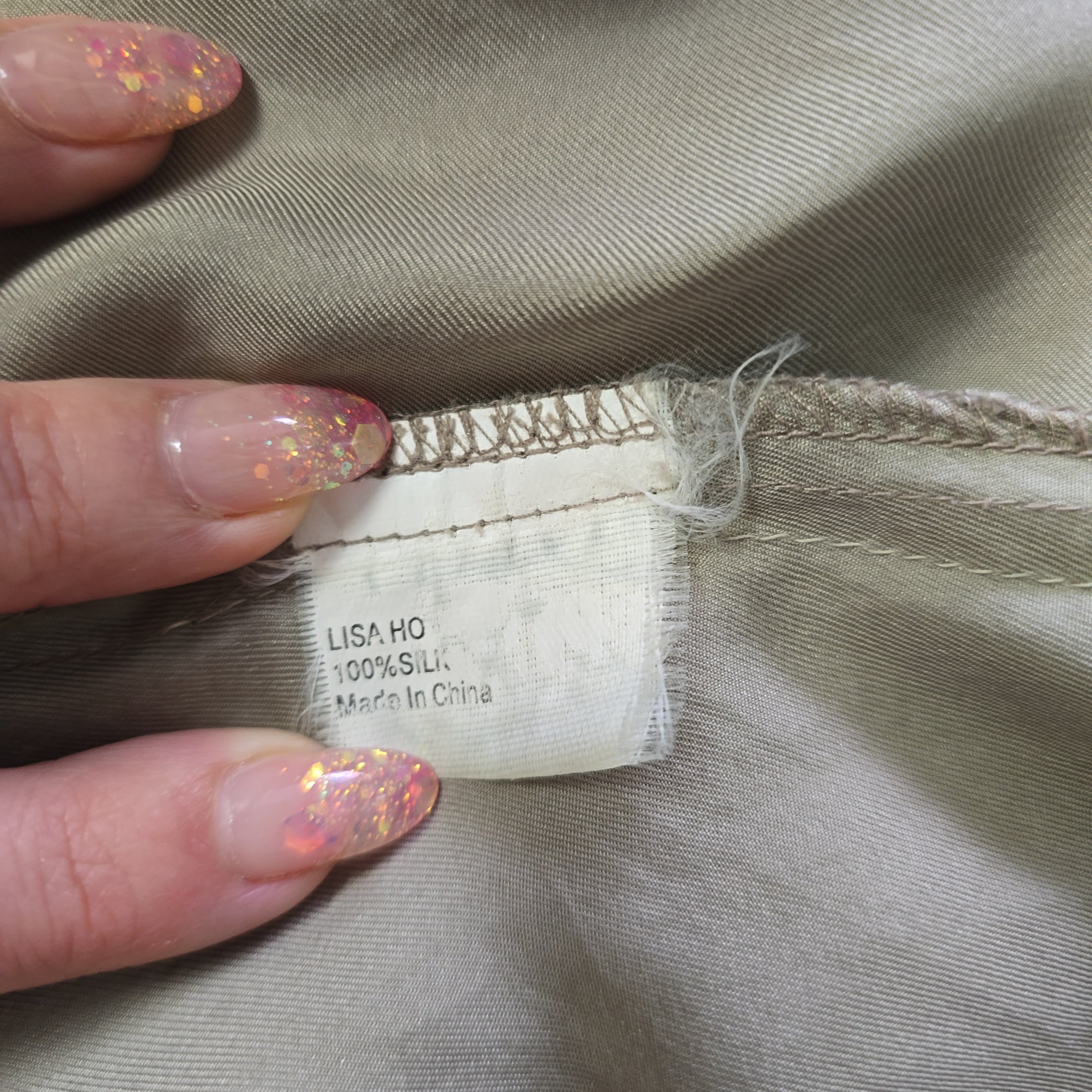 Close-up of a clothing tag on beige fabric with a hand holding it.