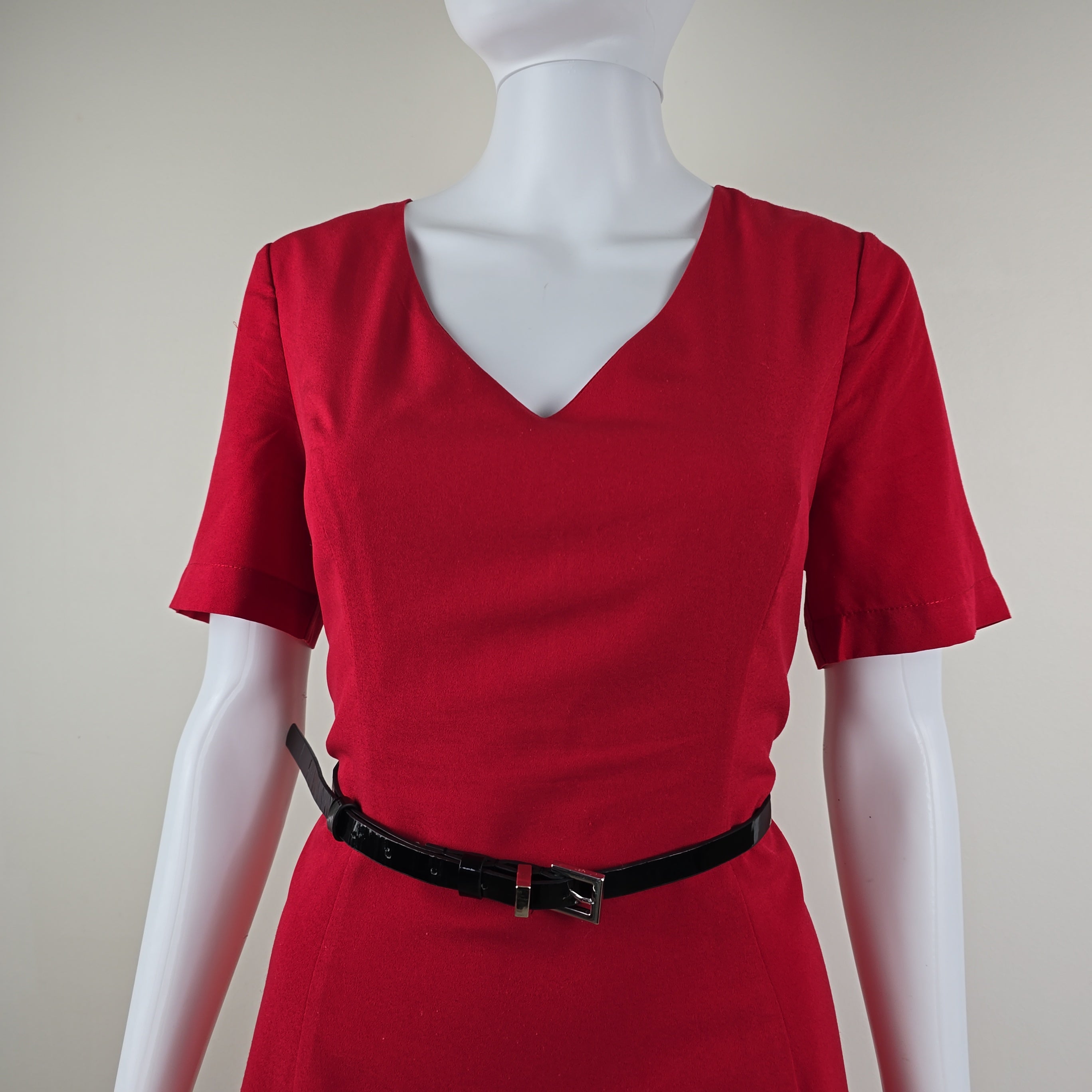 Red dress with a black belt on a mannequin against a plain background