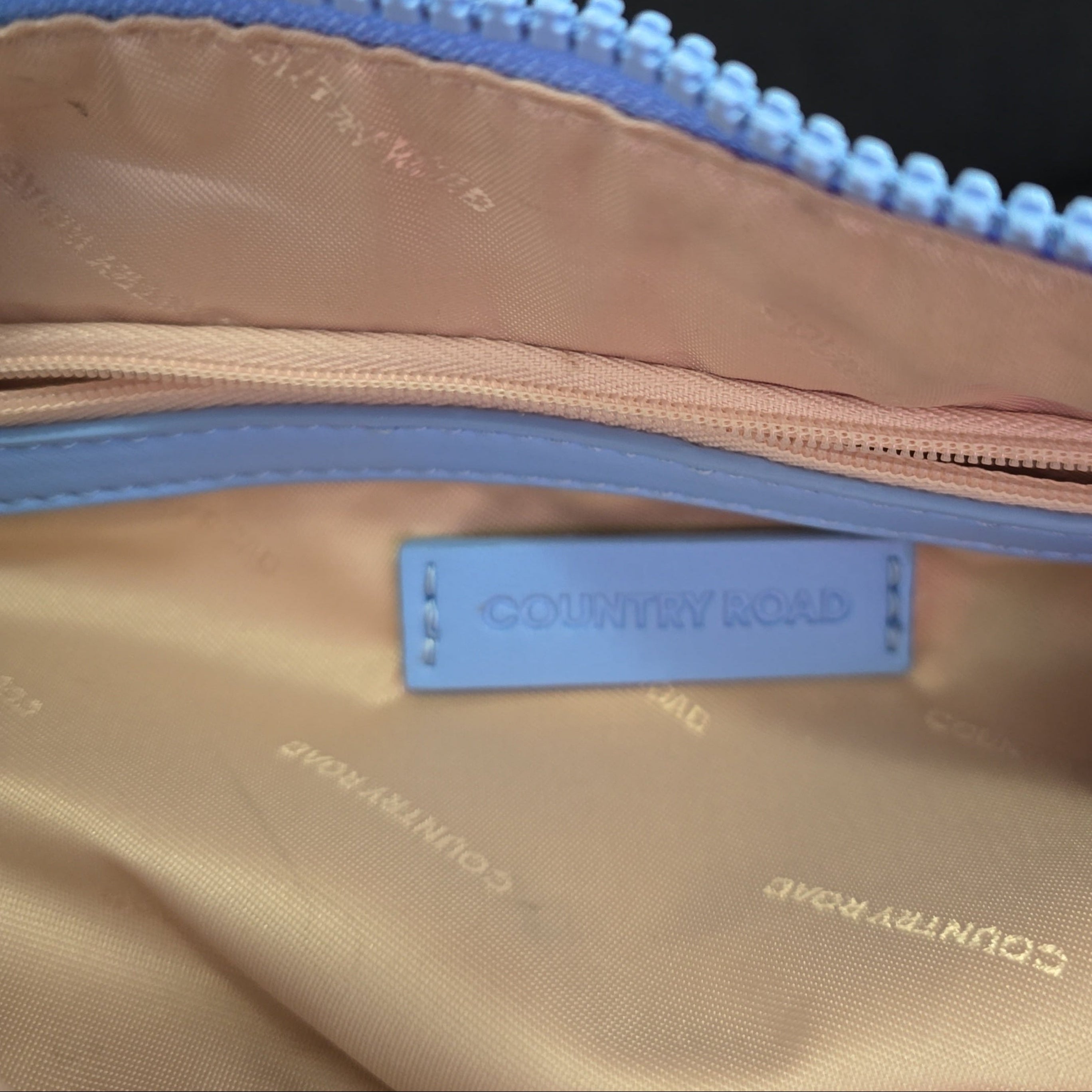 Close-up of a blue bag with a blue zipper and visible brand label on a light background