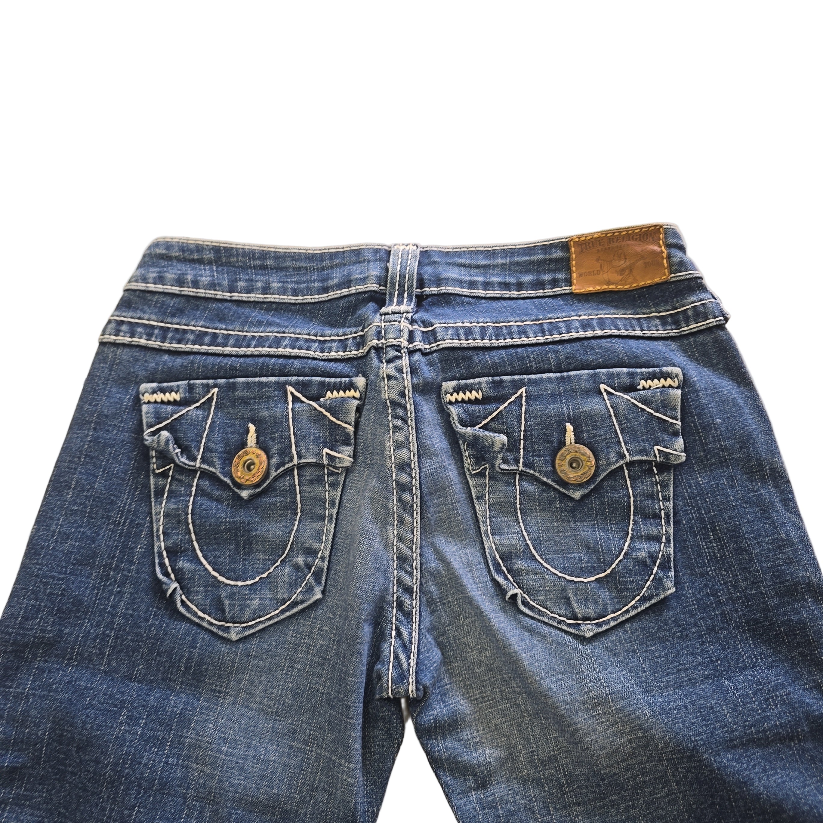 Close-up of blue jeans with button and back pocket details on a light background