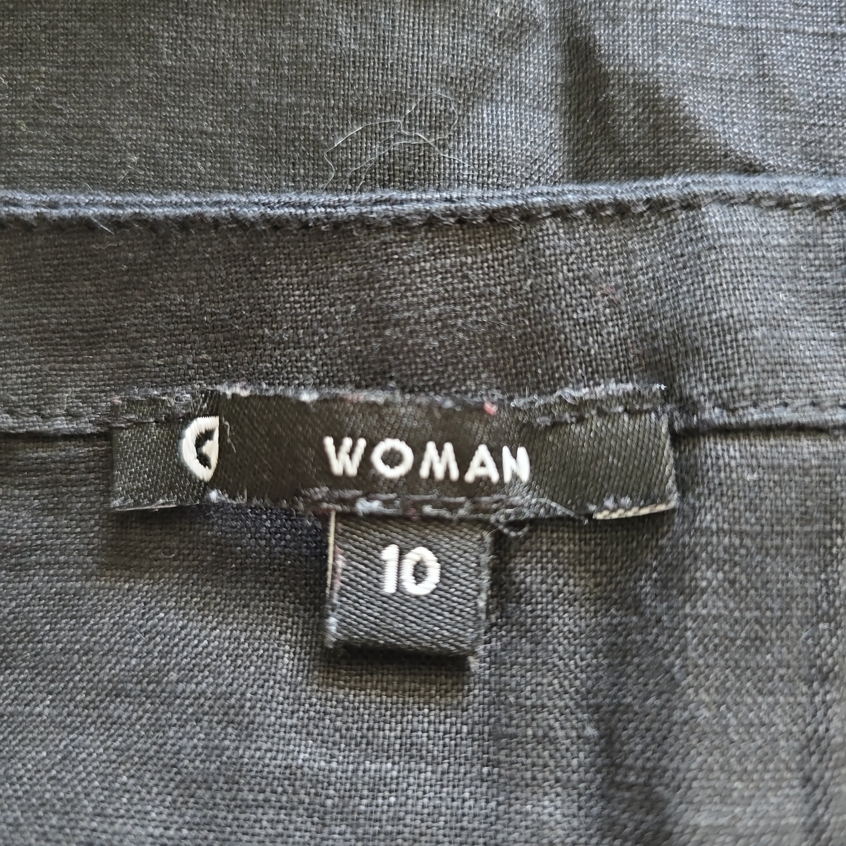 Clothing tag on a gray fabric with 'WOMAN' and size '10' printed on it.