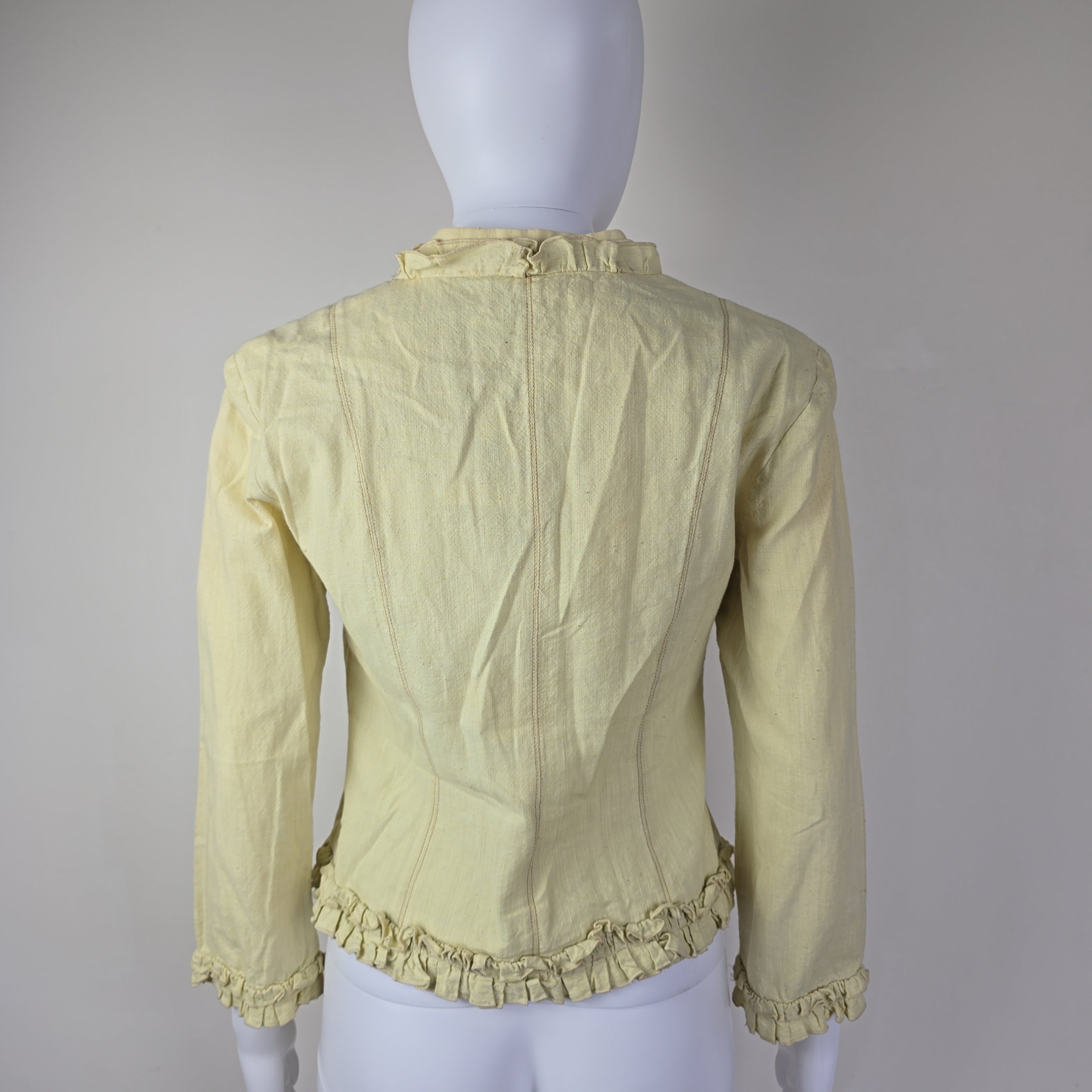 Light yellow jacket with frill details on a light background
