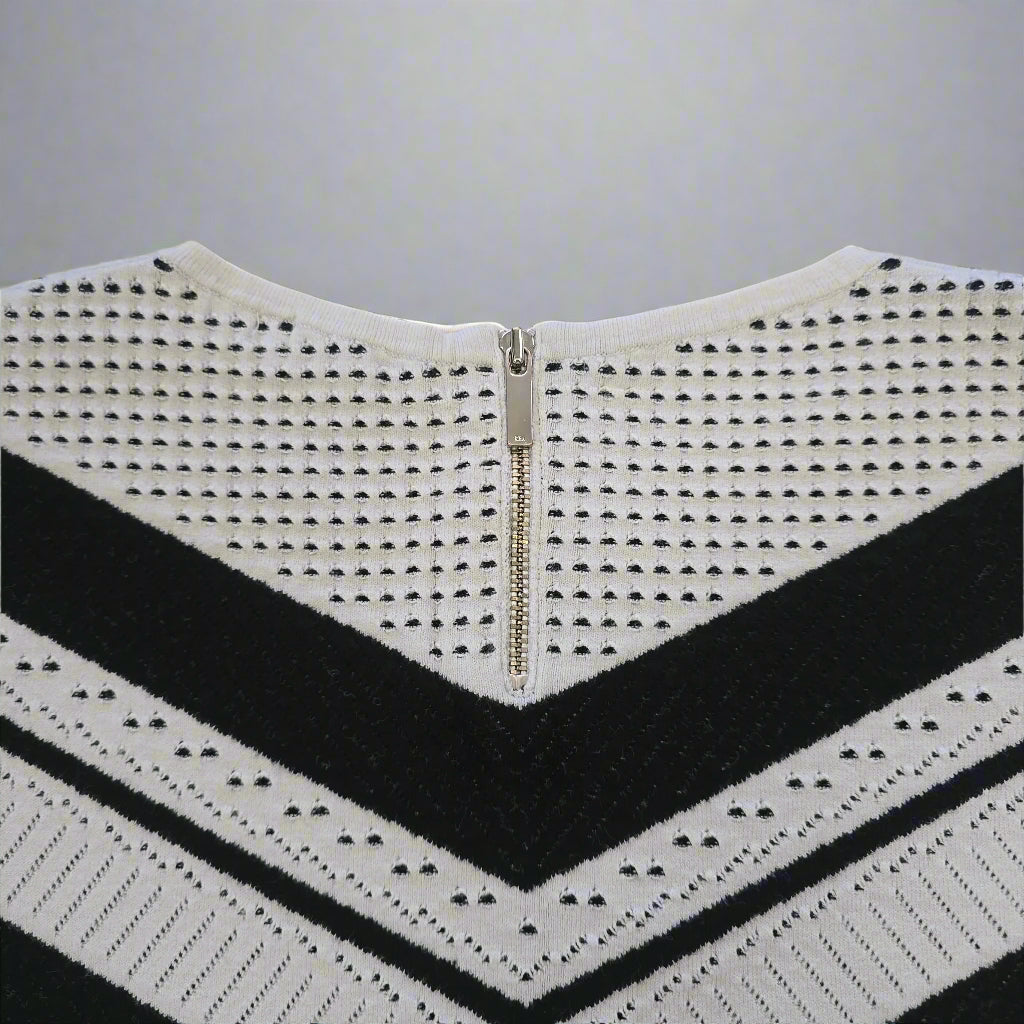 White knitted top with black stripes and a zipper on a beige background