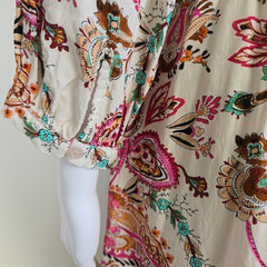 Close-up of a fabric with intricate floral and paisley patterns in brown, pink, and green on a beige background.