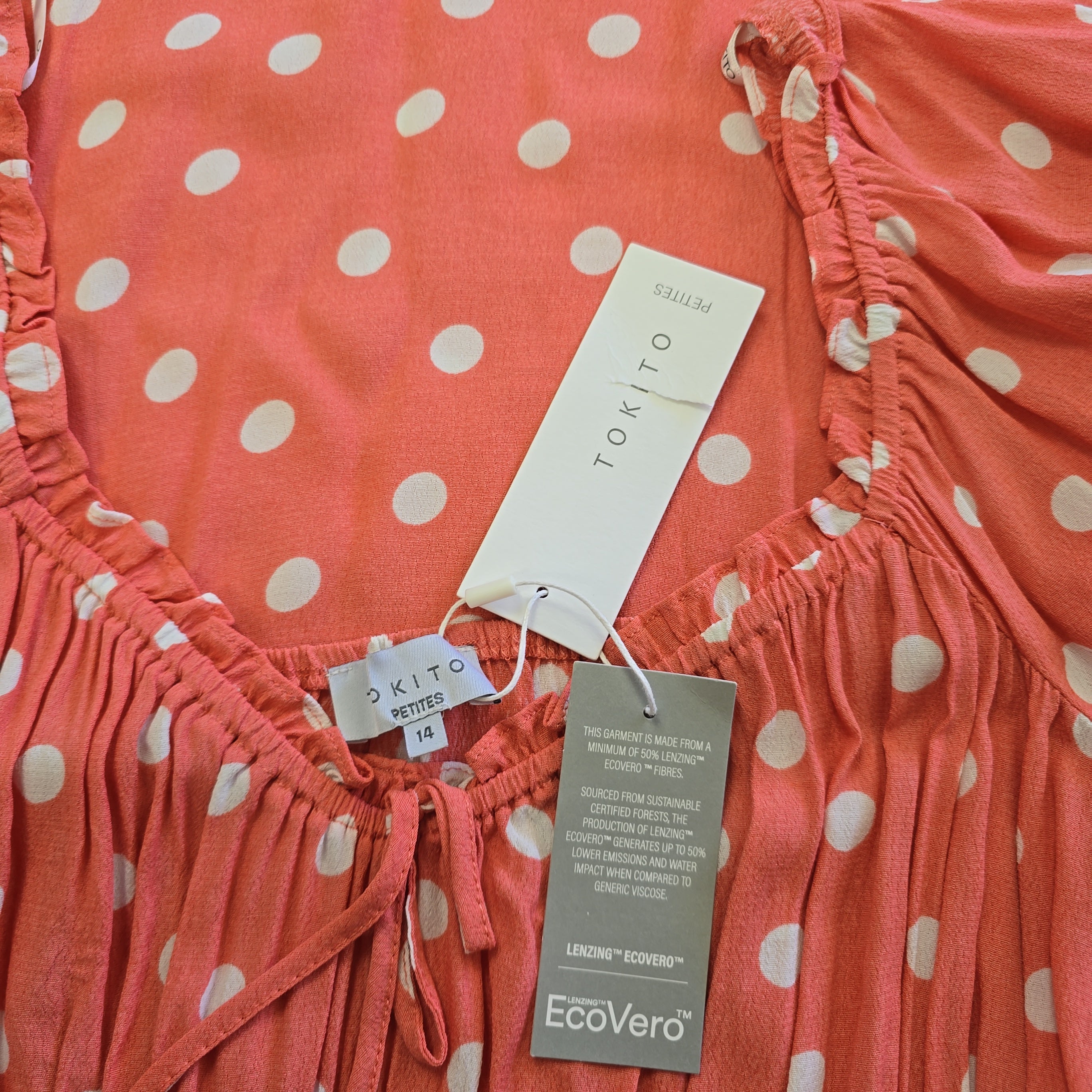 Coral polka dot dress with tags on a plain background
