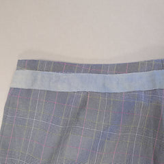Close-up of plaid fabric with a visible seam on a light gray background