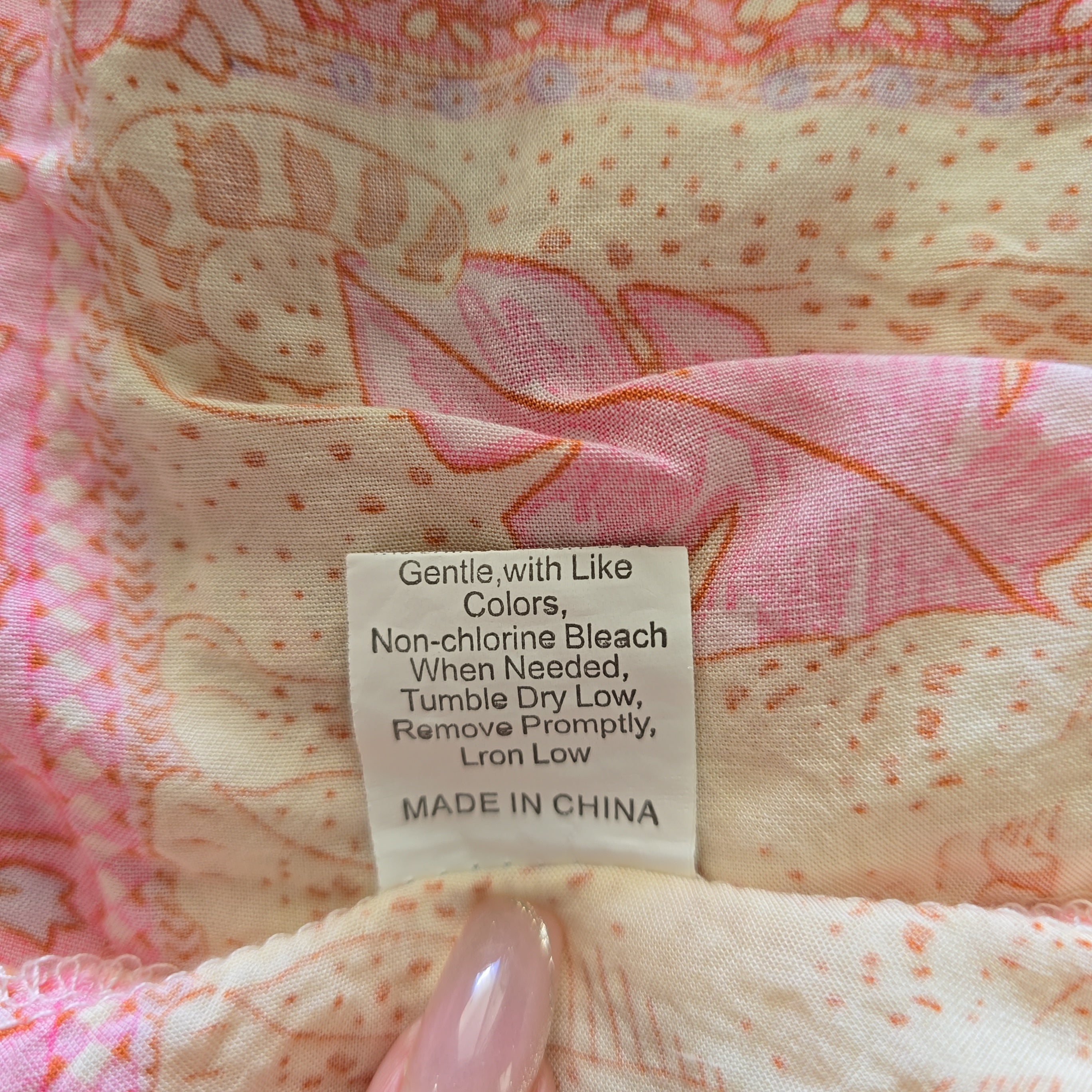 Fabric with a label indicating care instructions and origin, featuring pink and orange patterns.