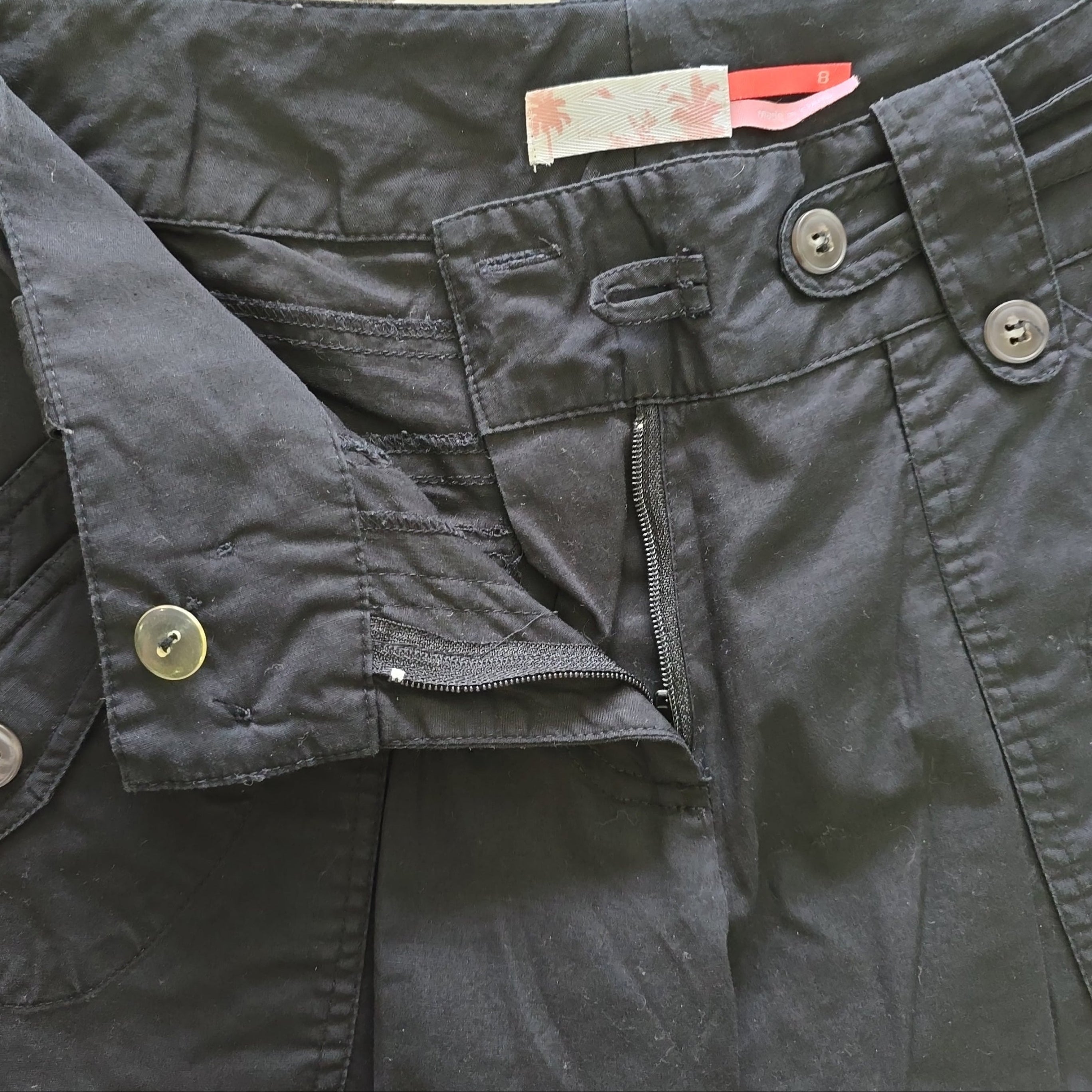 Black pants with buttons and a zipper, featuring a tag on a light background.