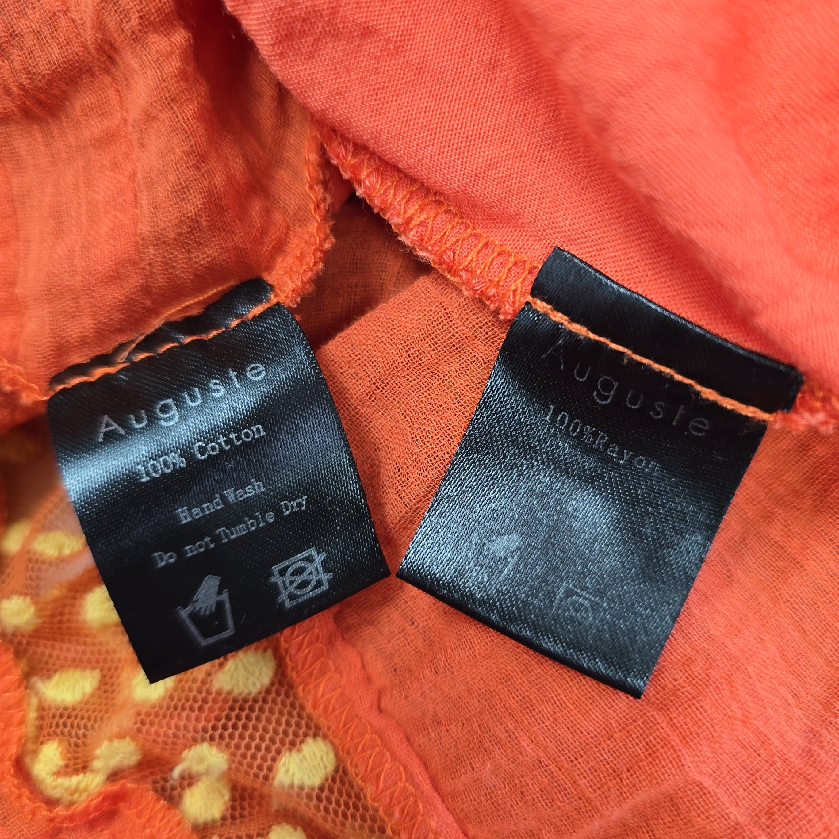 Two Auguste brand labels on orange fabric with visible text and symbols.