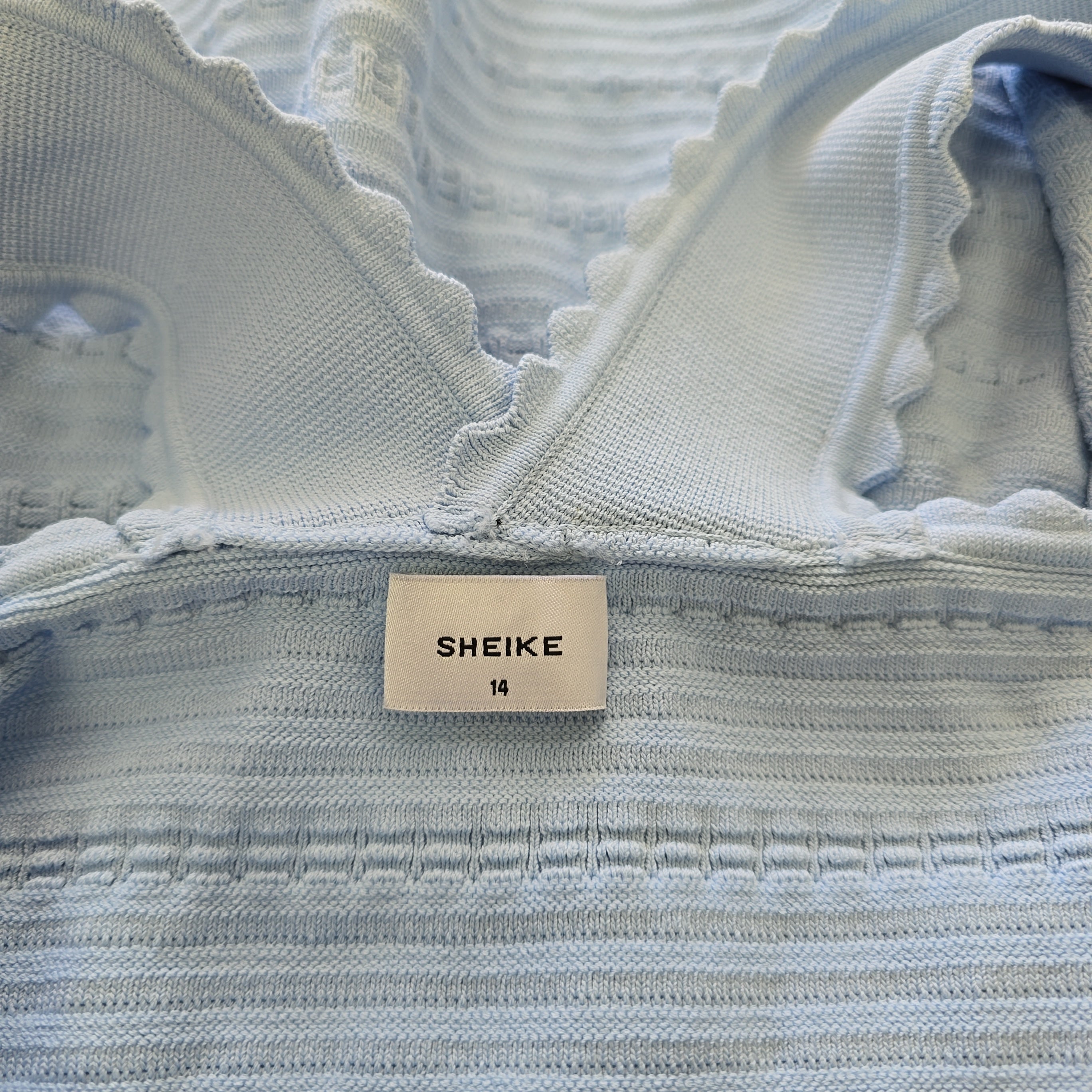 Close-up of a light blue textured fabric with a 'SHEIKE' label.