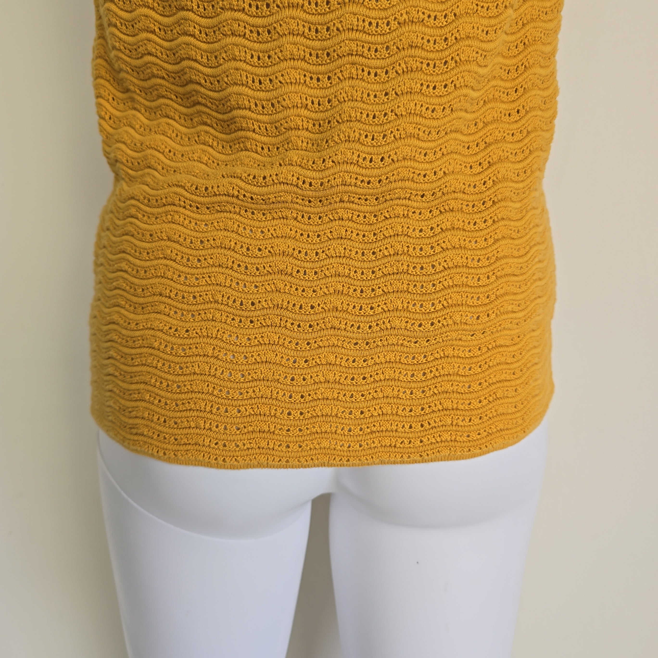 Mannequin wearing a mustard yellow knitted garment on a beige background