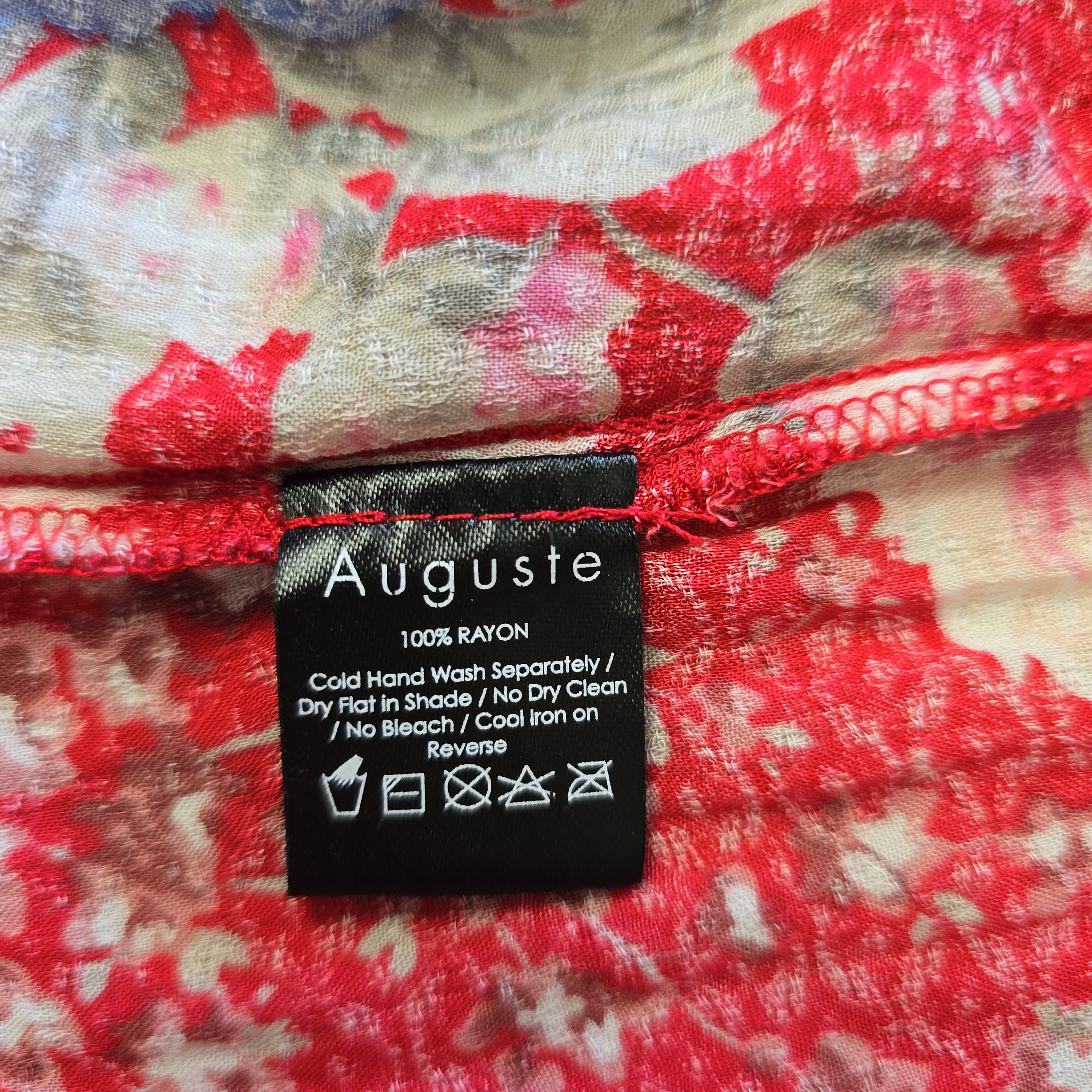 Clothing label on a red floral fabric with 'Auguste' branding.