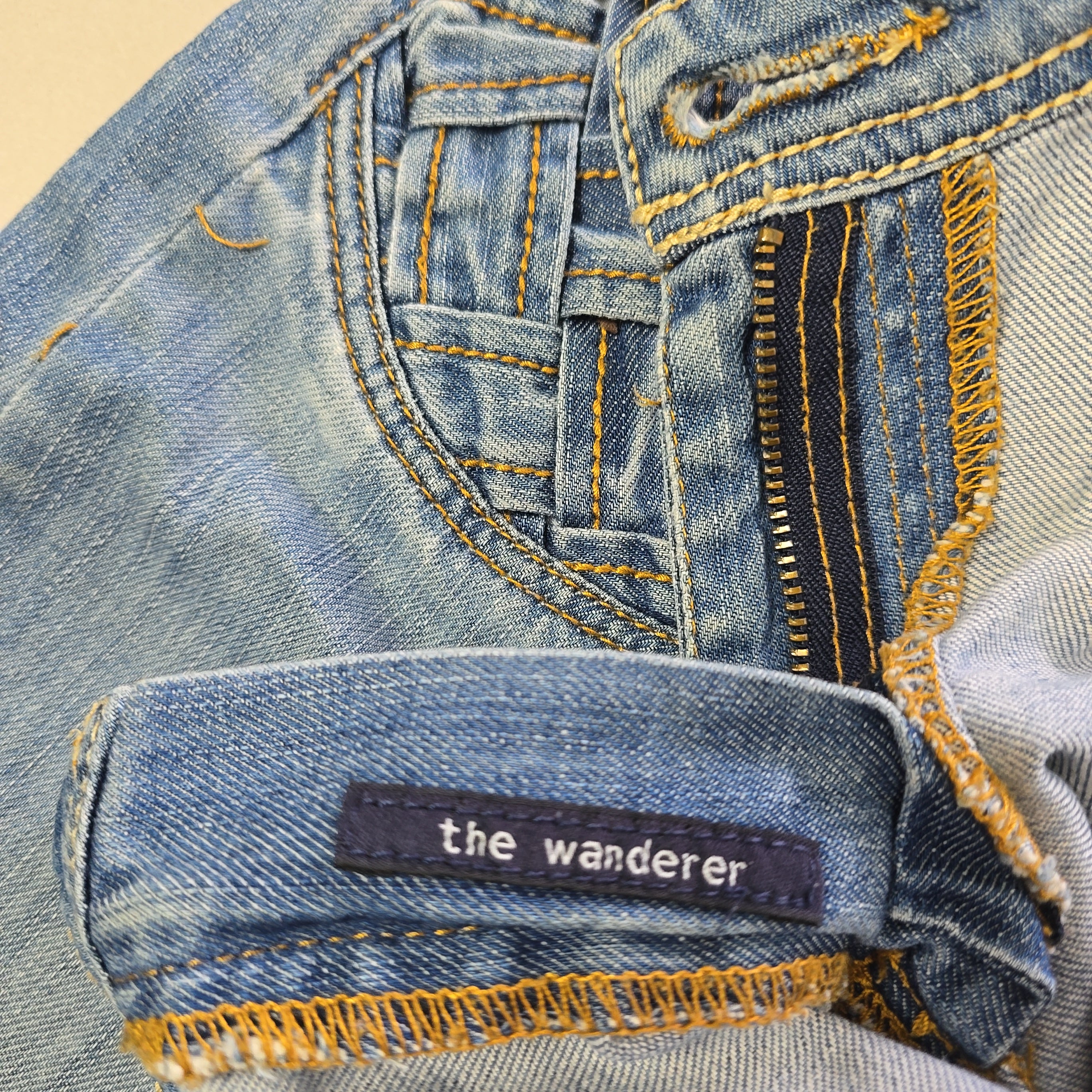 Close-up of blue denim jeans with 'the wanderer' label.