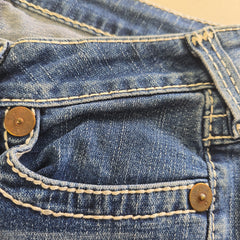Close-up of a blue denim with gold buttons and stitching details.