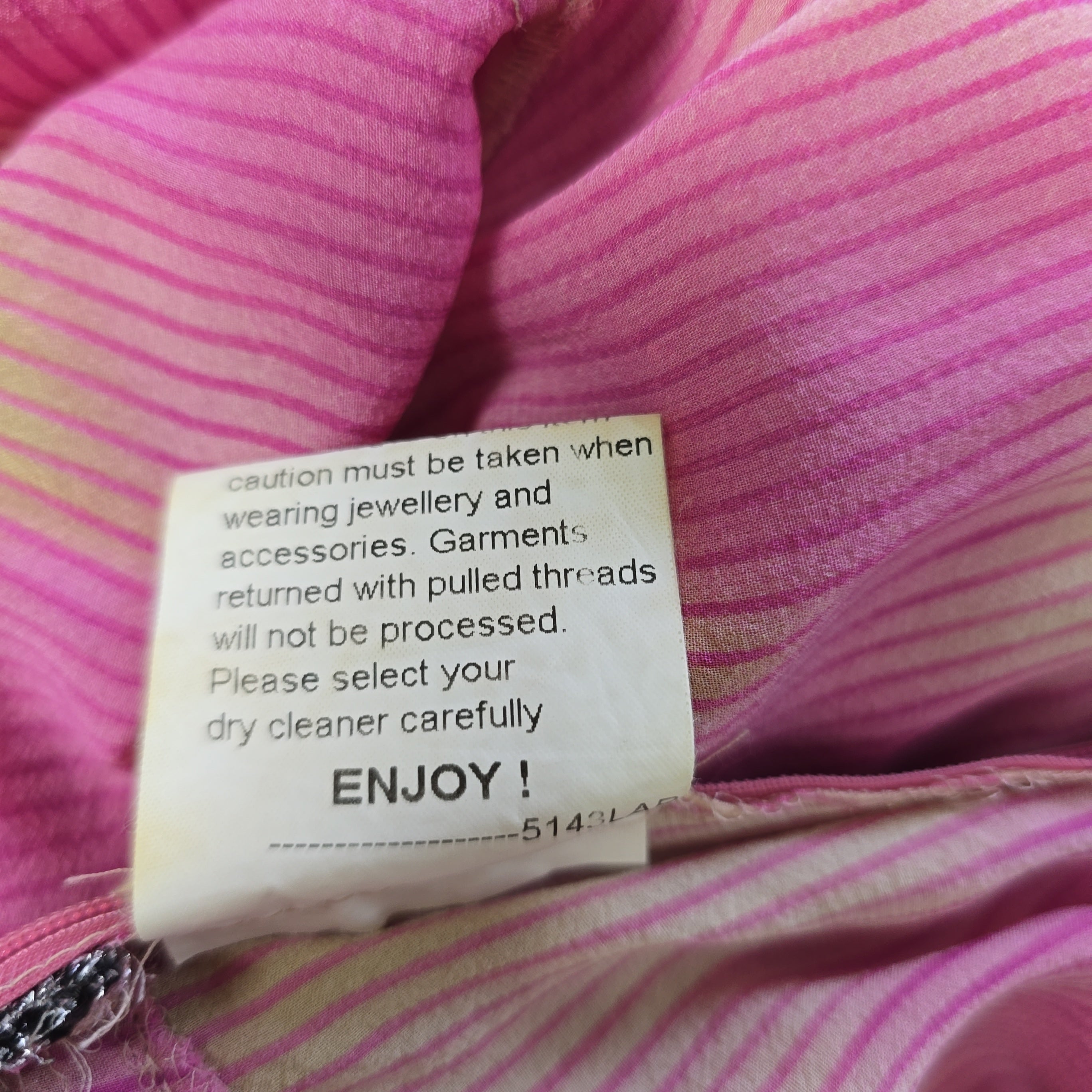 Close-up of a clothing tag on a pink striped garment with text.