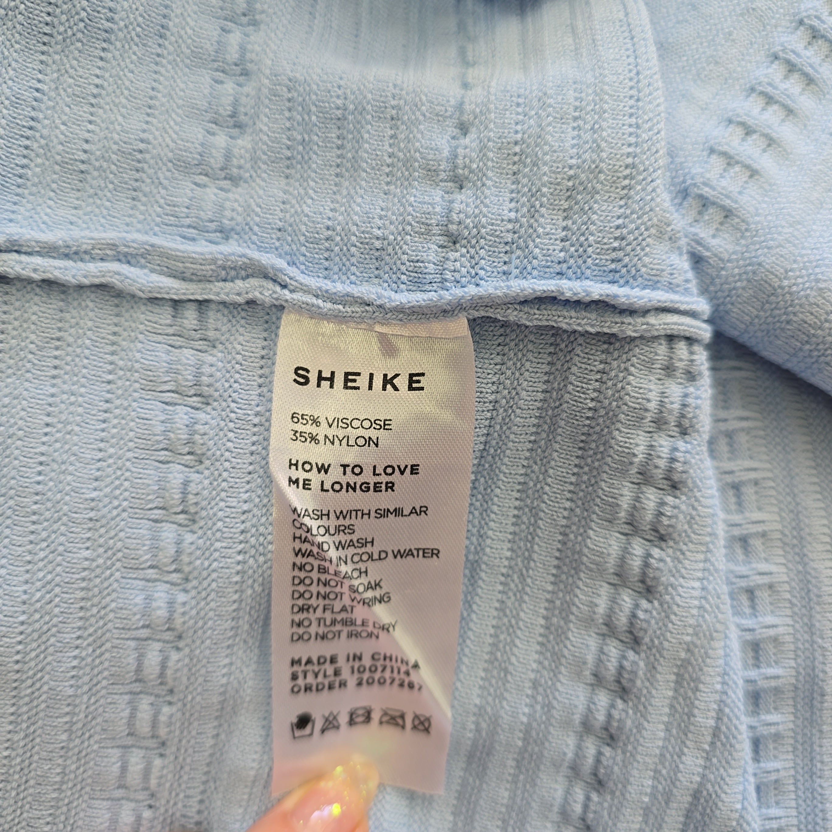 Close-up of a label on a piece of light blue fabric with 'SHEIKE' branding.
