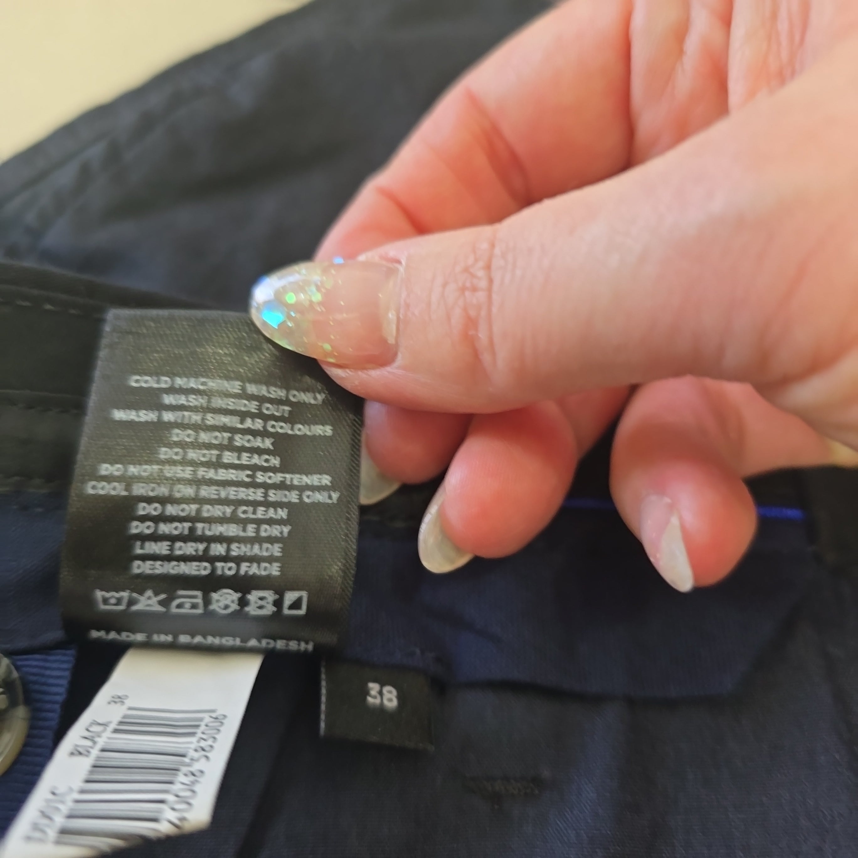 Close-up of a hand holding a clothing label with text and a brand logo.