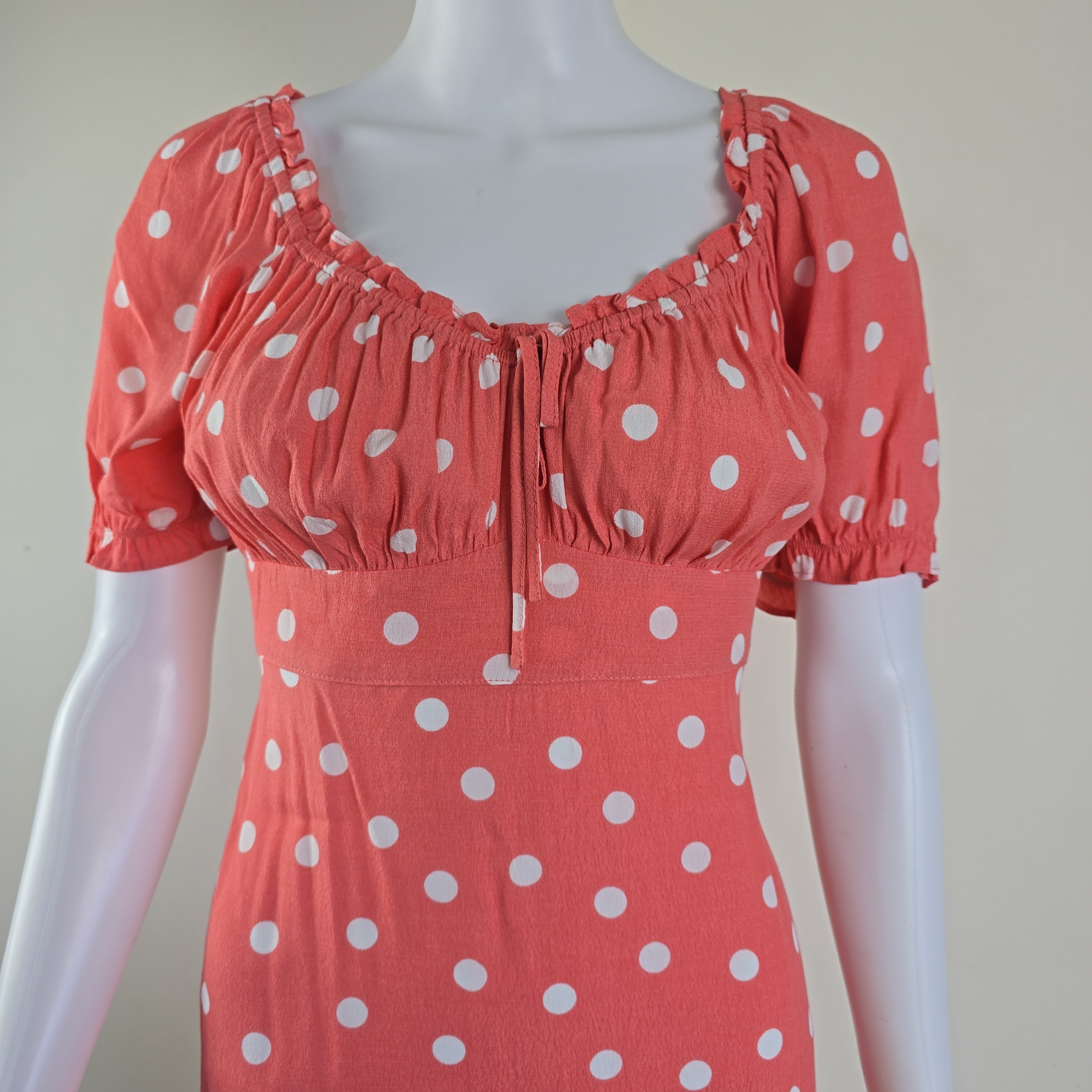 Mannequin wearing a coral dress with white polka dots on a plain background