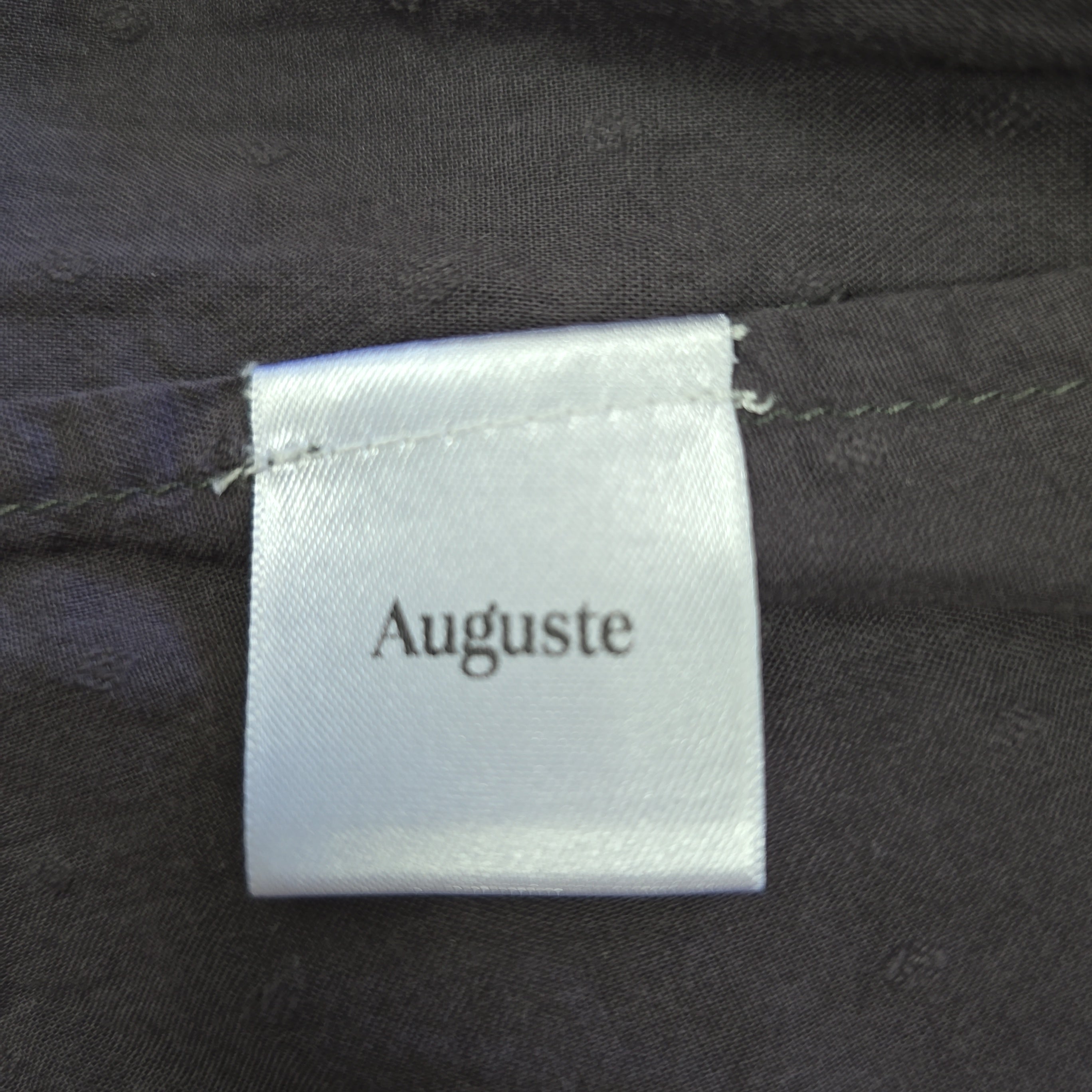Clothing label with 'Auguste' text on a dark fabric background