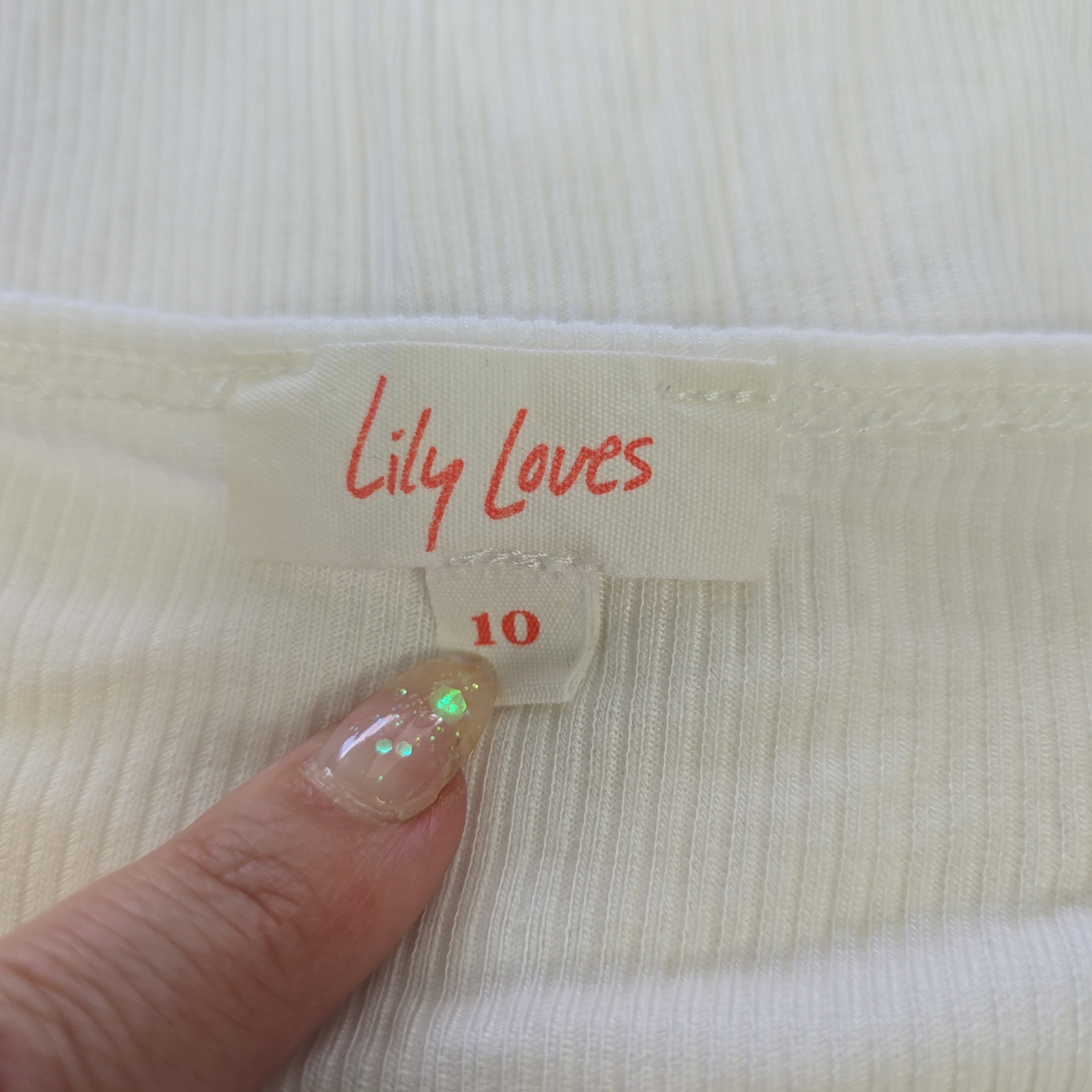 Close-up of a label on a garment with 'Lily Loves' text, held by a hand.