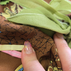 Close-up of fabric with green and brown patterns held by a hand.