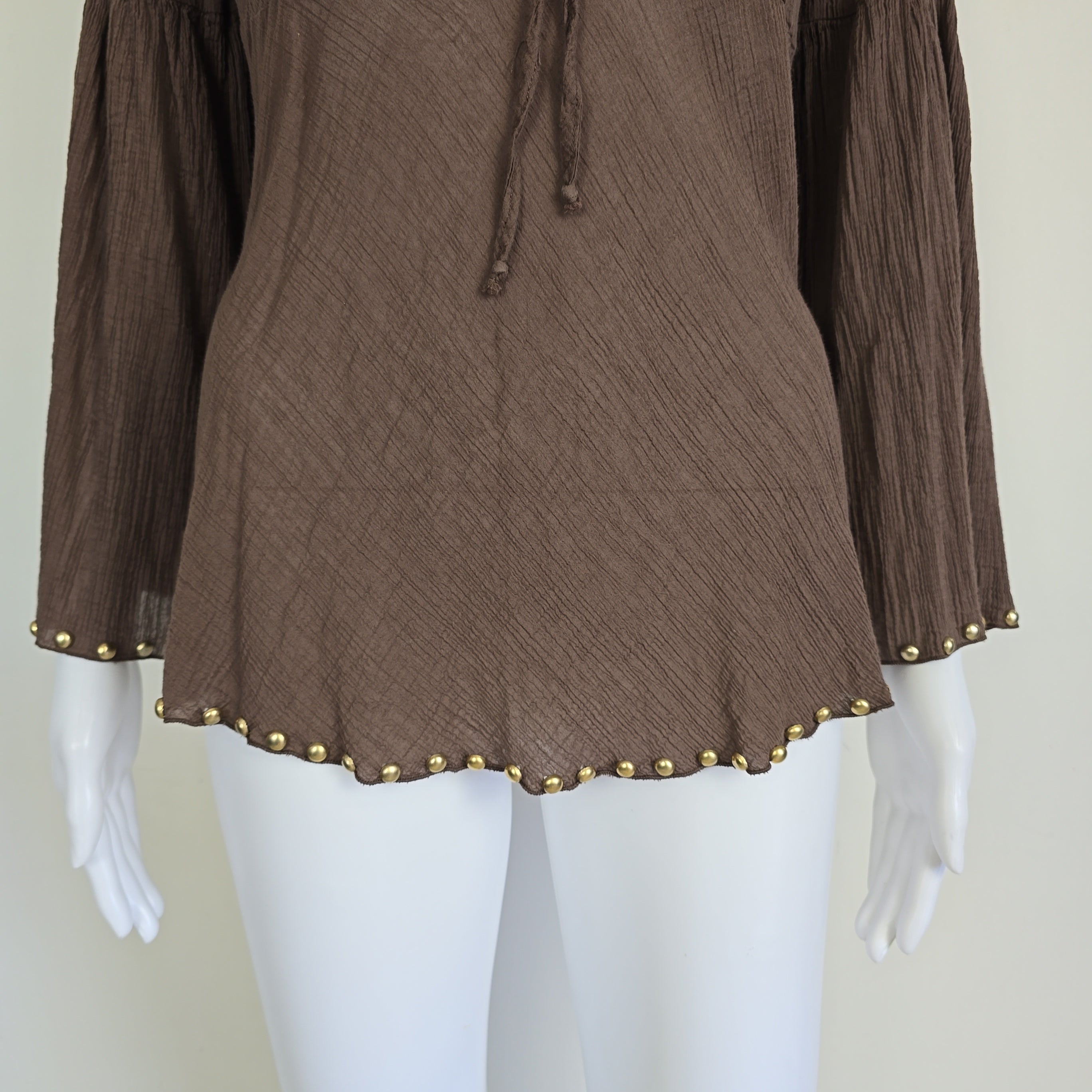 Brown fabric with gold studs on a mannequin arm against a white background