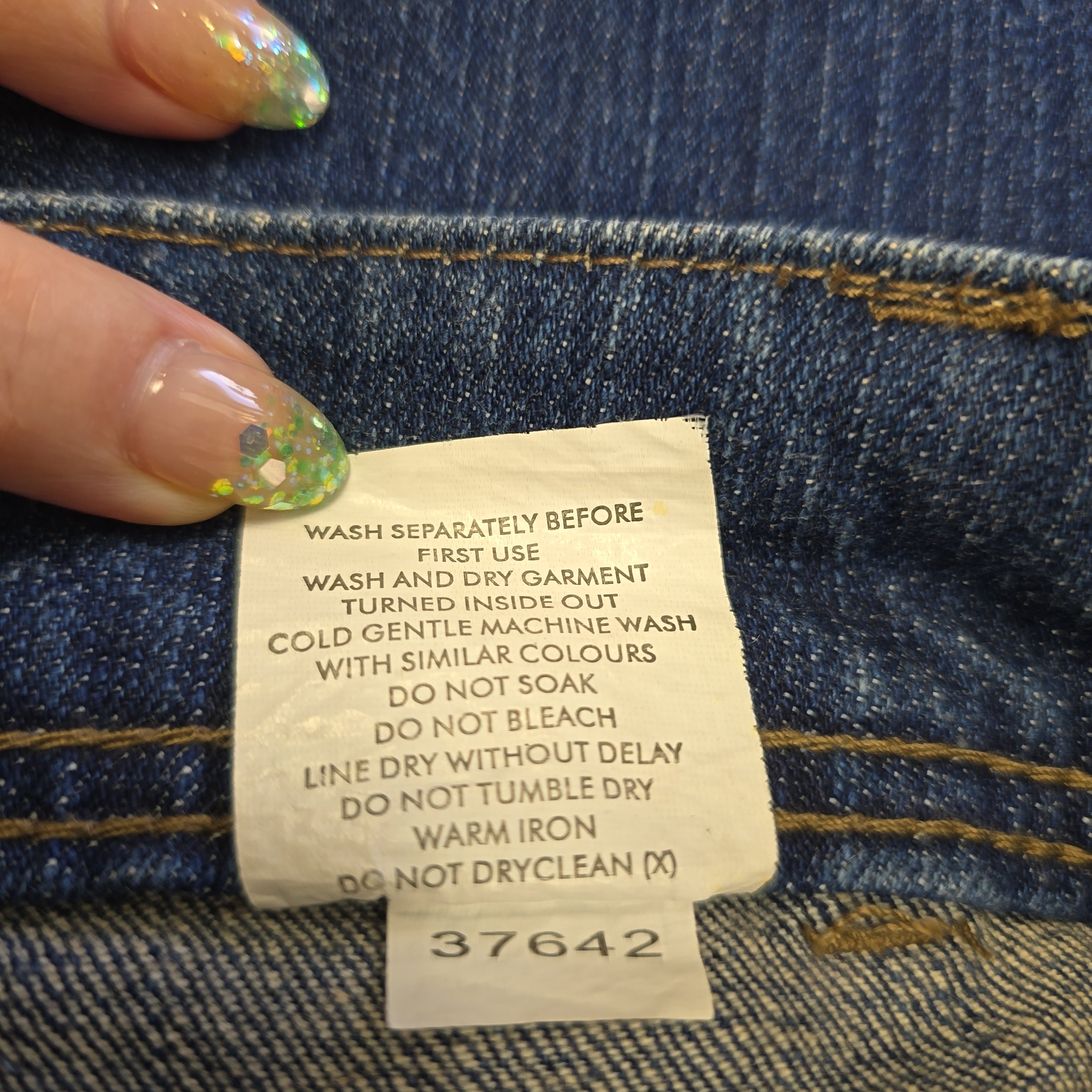 Close-up of a clothing label on denim fabric with a hand holding it.