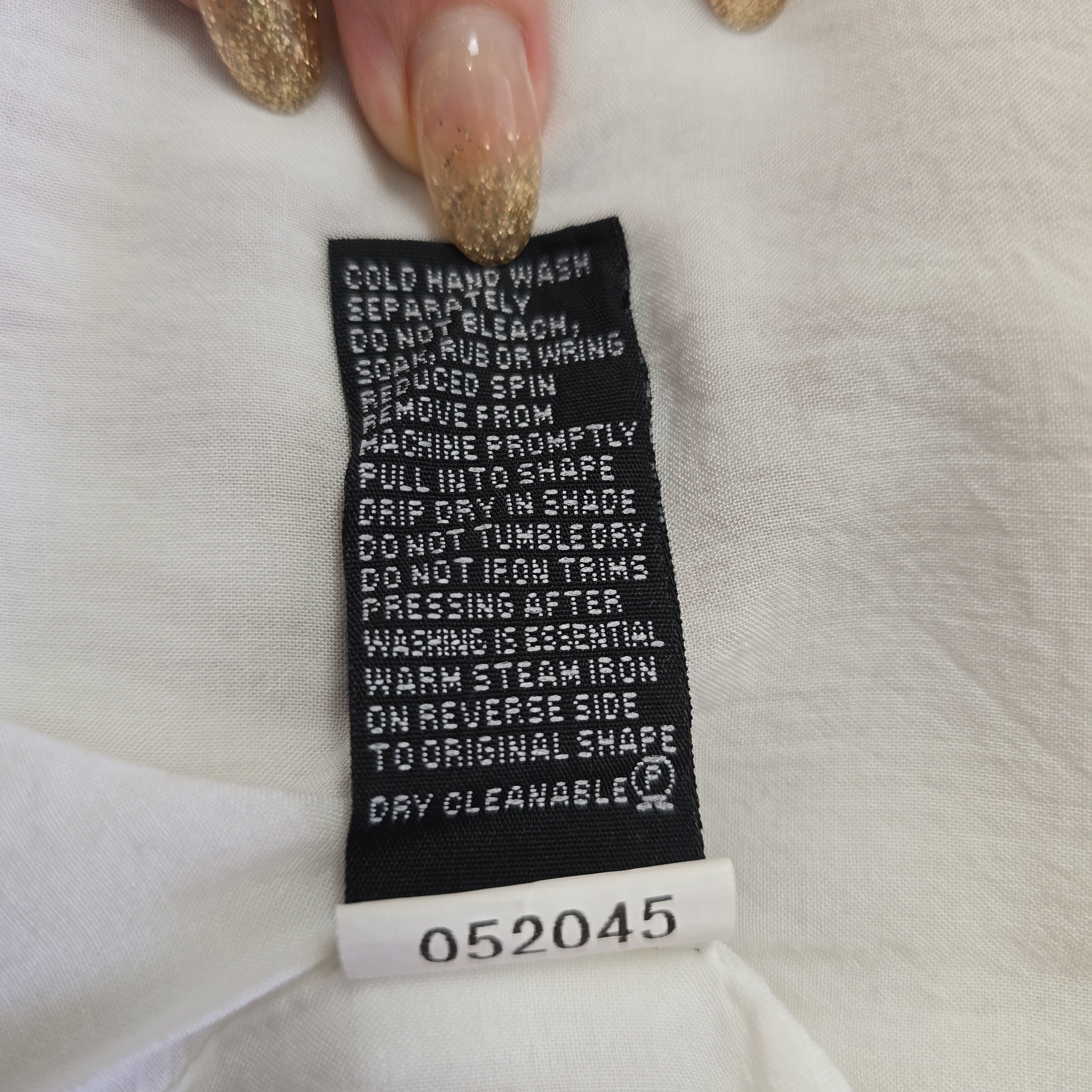 Clothing label on a white garment with text and numbers.
