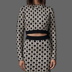 Model wearing a black and white patterned outfit with sunglasses on a plain background