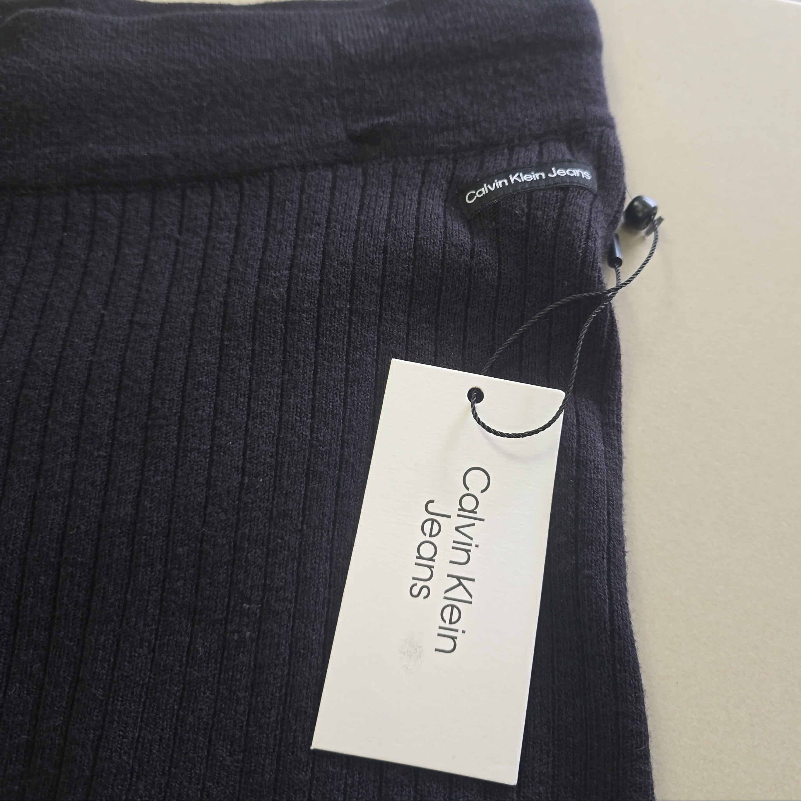 Black ribbed knit garment with a Calvin Klein Jeans tag on a beige background