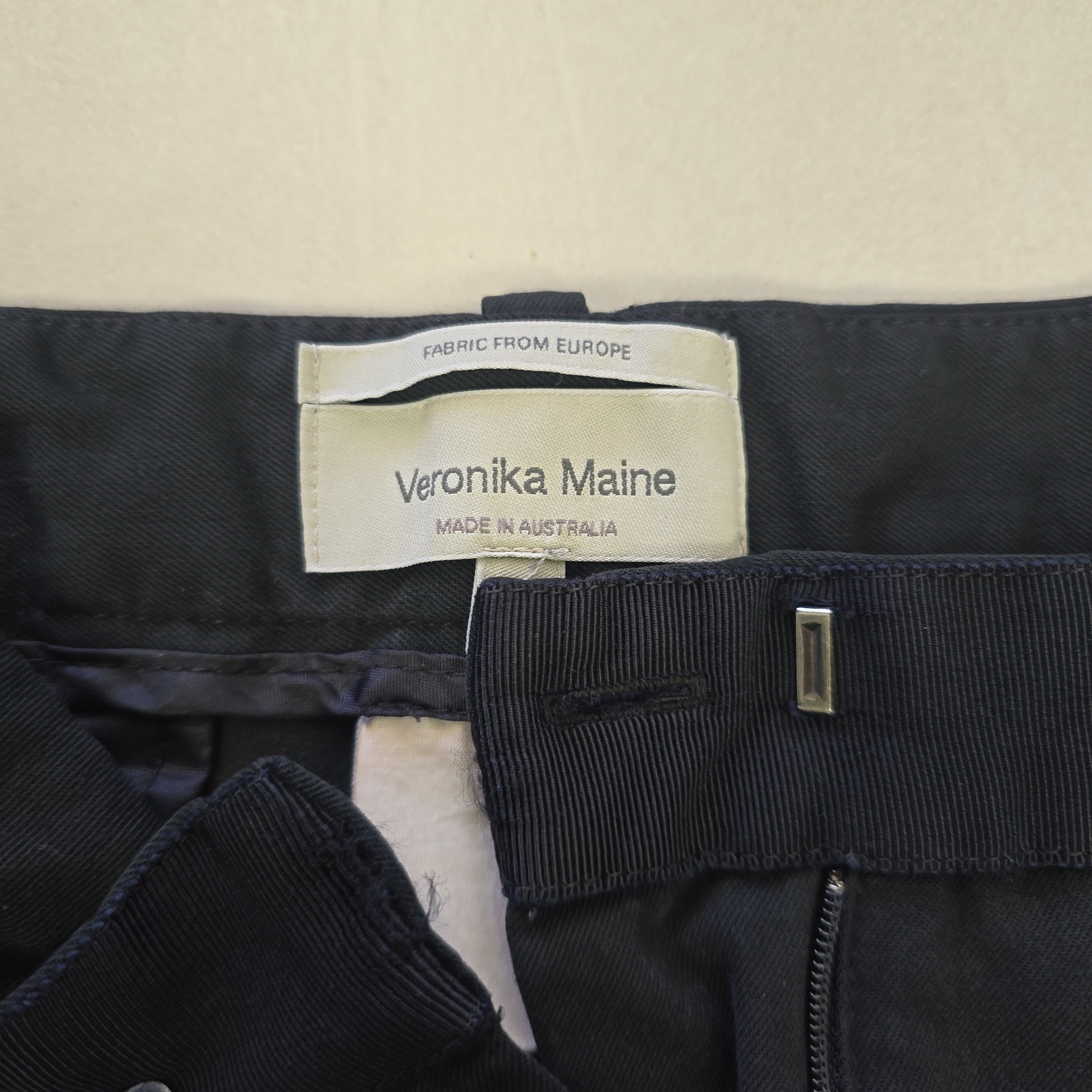 Close-up of a black Pants with a Veronika Maine label on a beige background