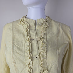 Light-colored jacket with ruffled details on a mannequin against a white background