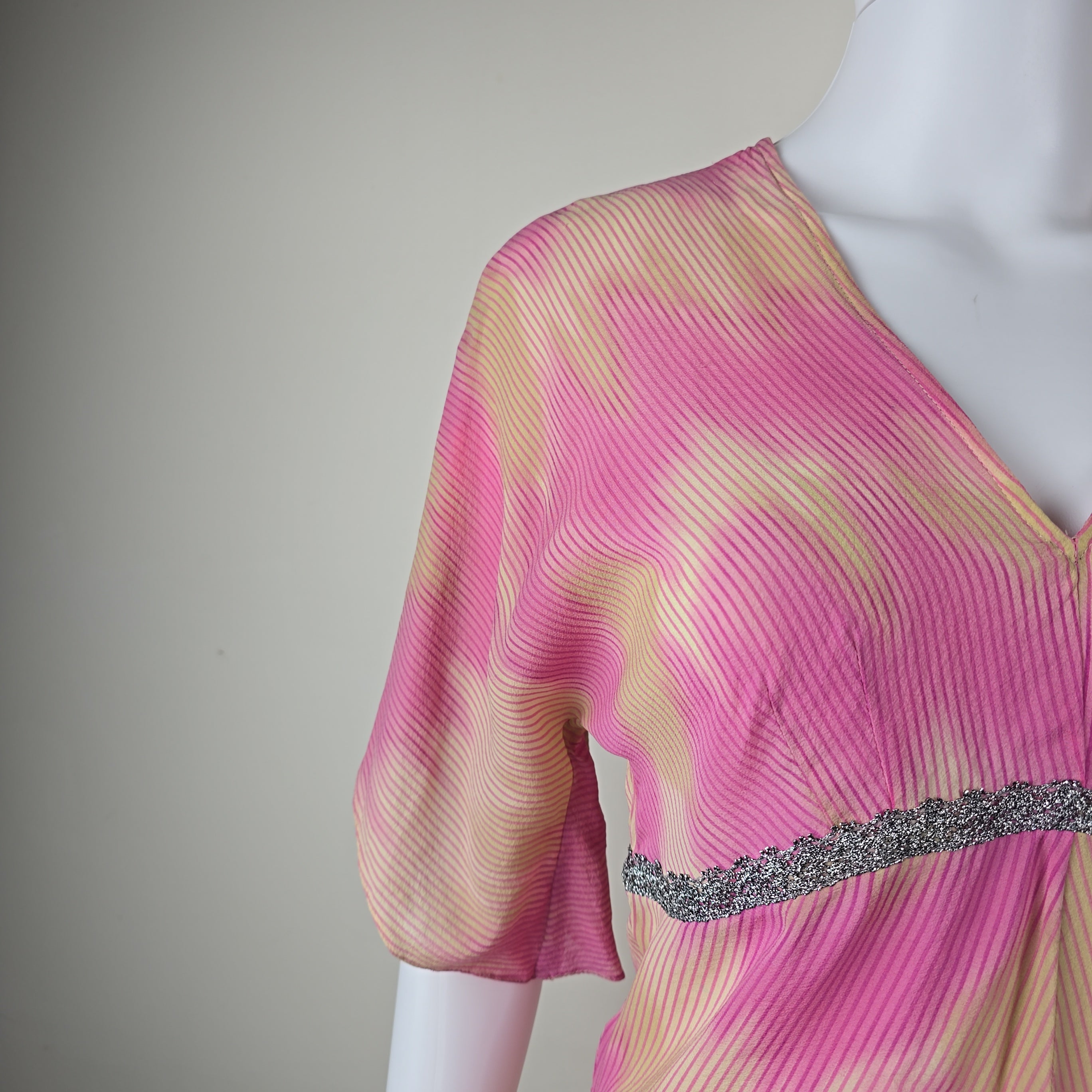 Close-up of a pink and gold textured fabric with a silver lace on a gray background