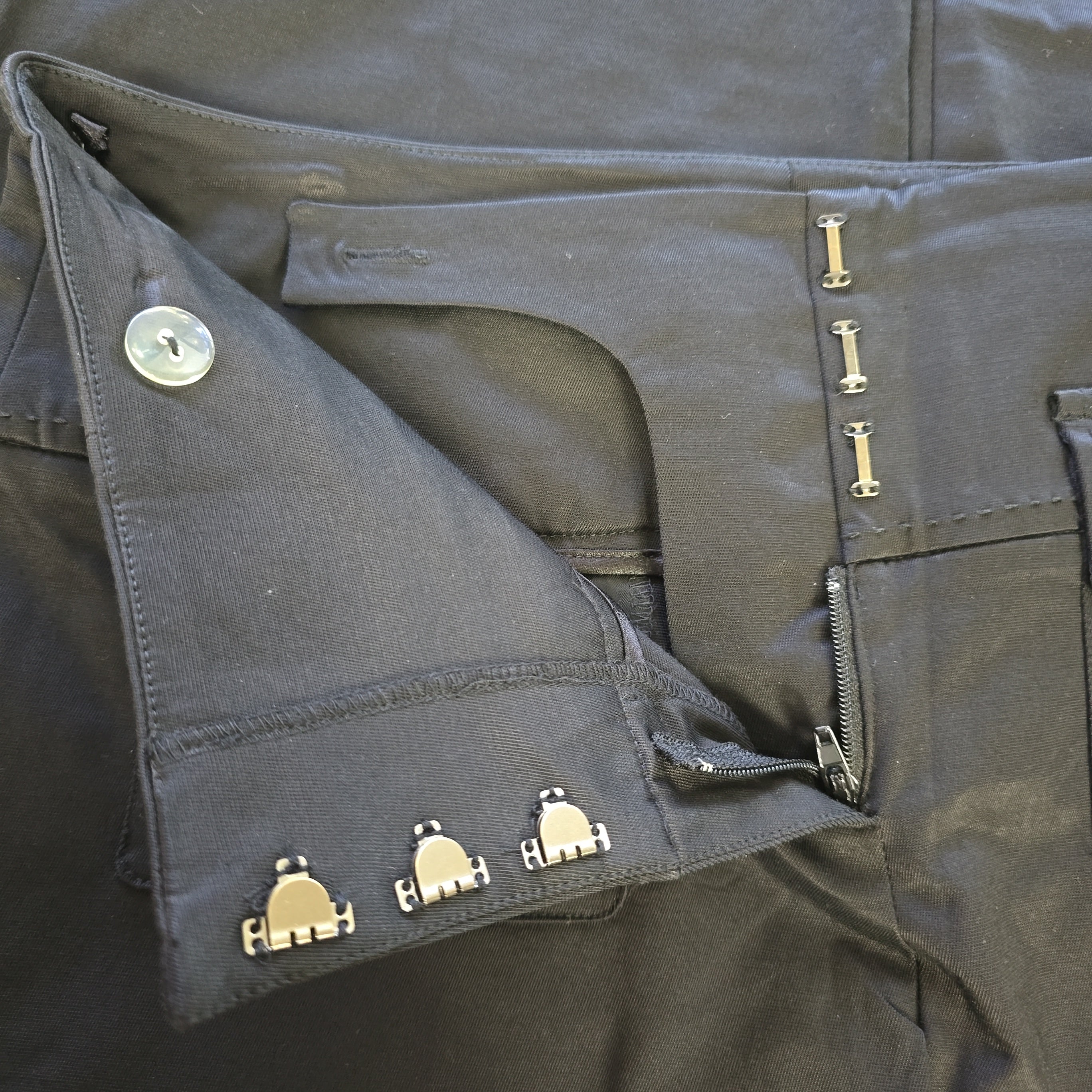 Close-up of black pants with silver buttons and zippers.
