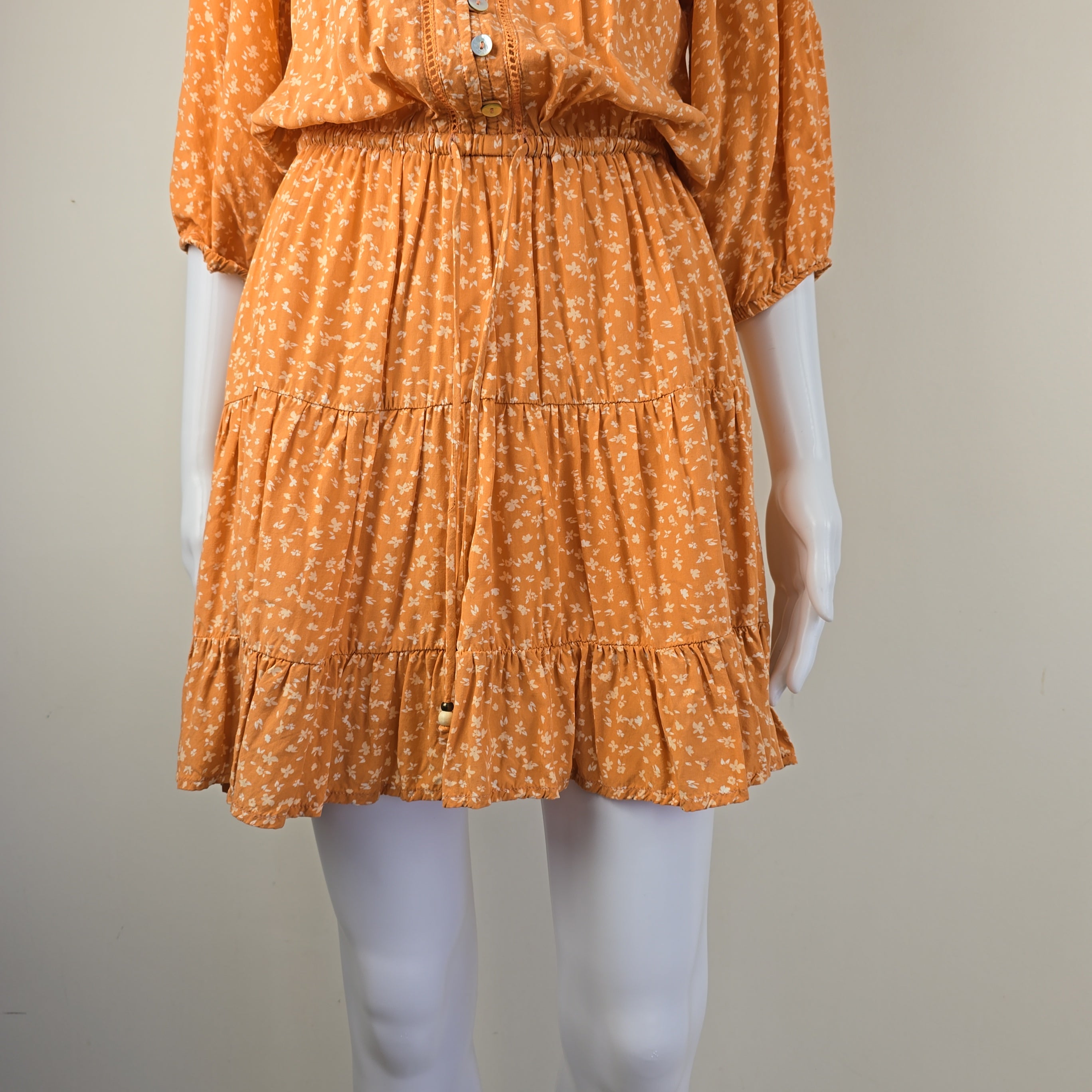 Orange dress with white flowers on a mannequin against a neutral background