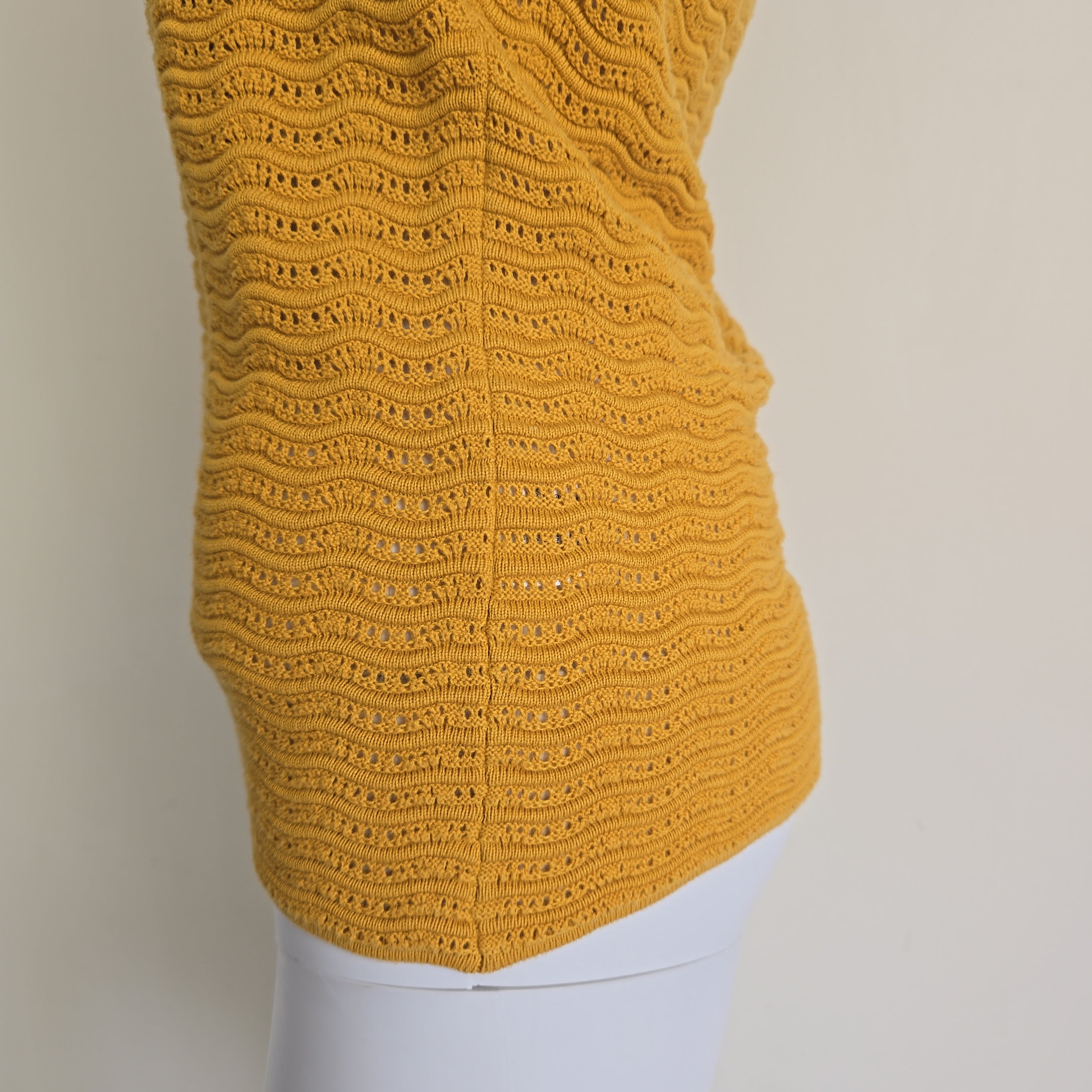 Yellow knitted sleeve on a mannequin against a neutral background