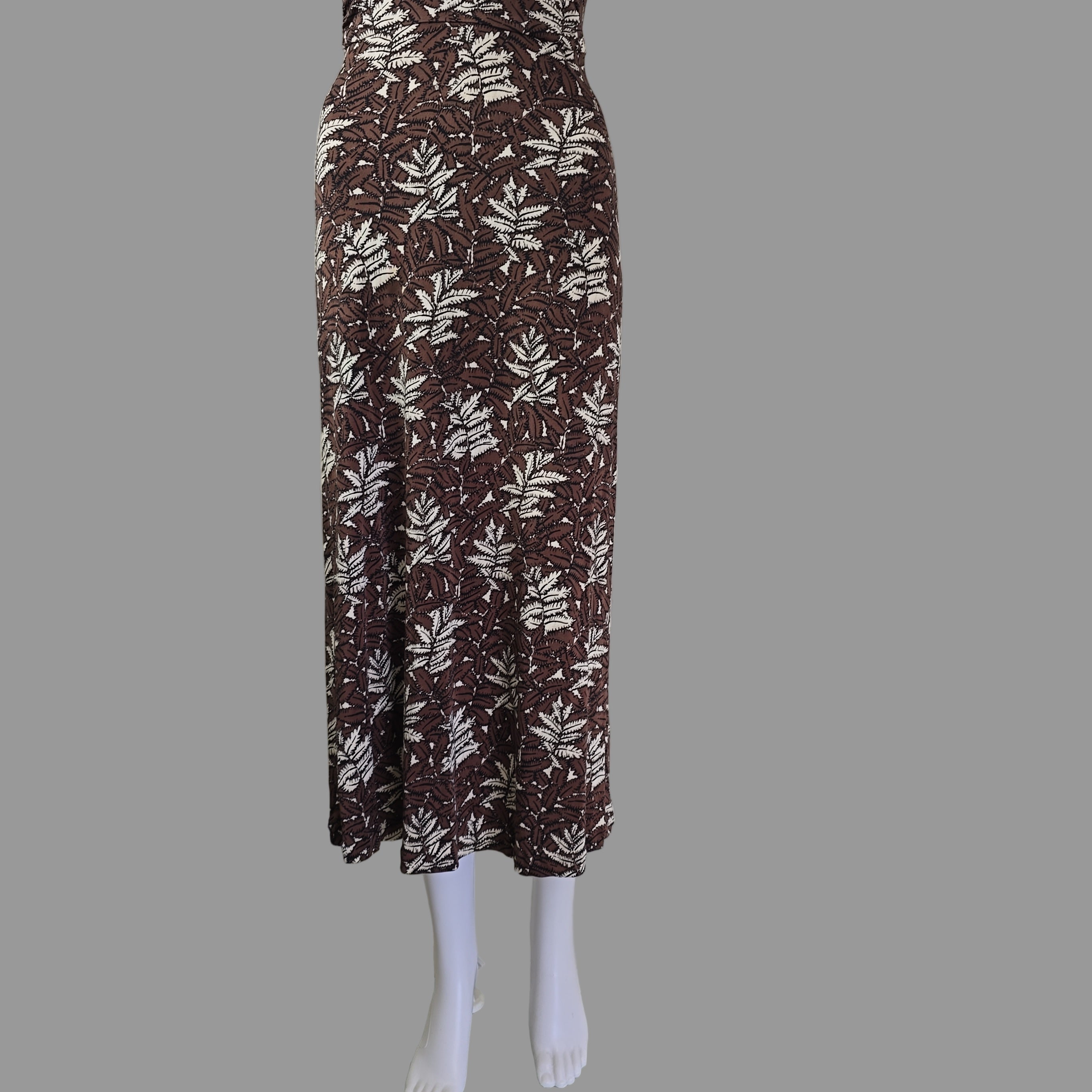 Folded brown fabric with leaf pattern on a mannequin arm against a white wall.