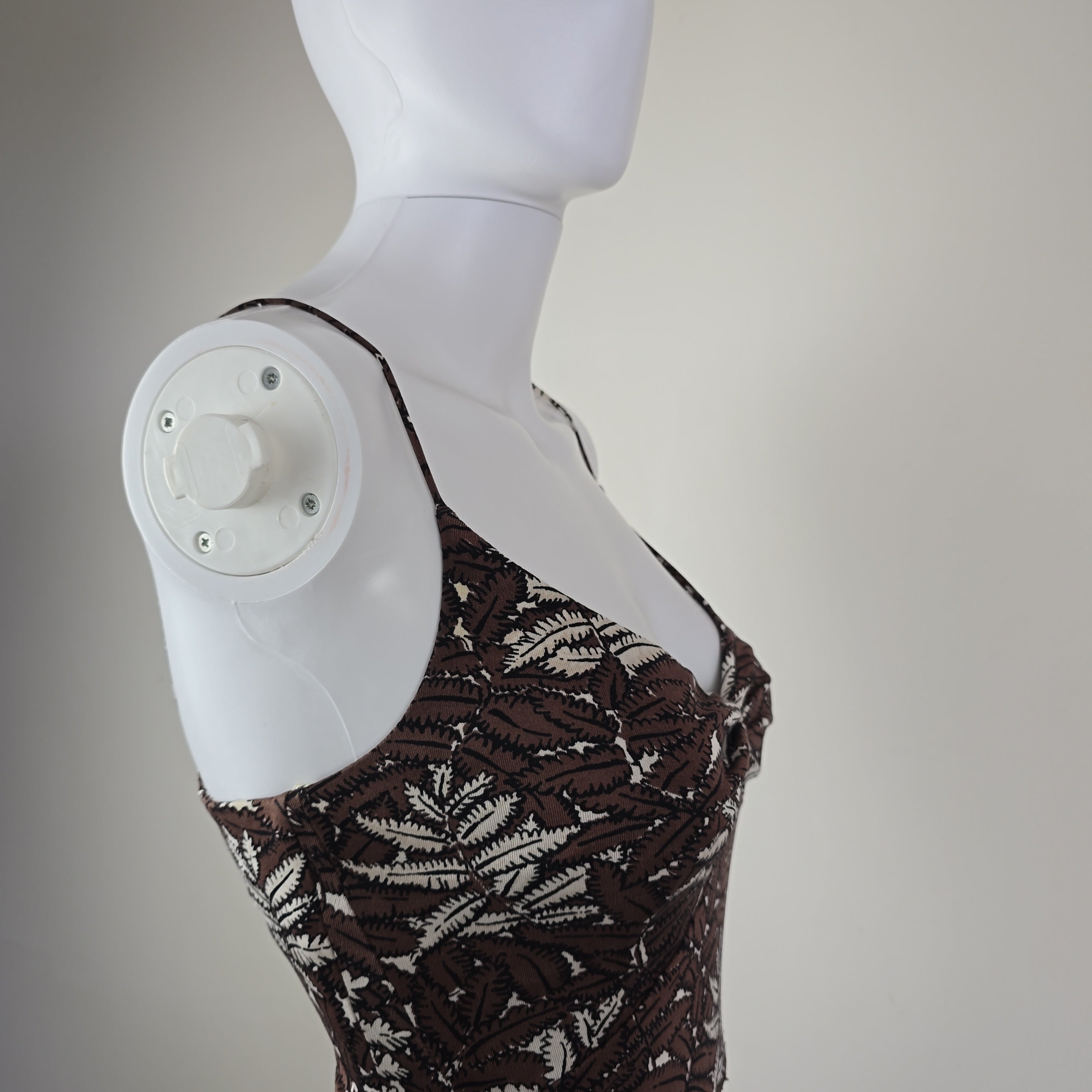 Mannequin arm with a brown patterned dress on a plain background