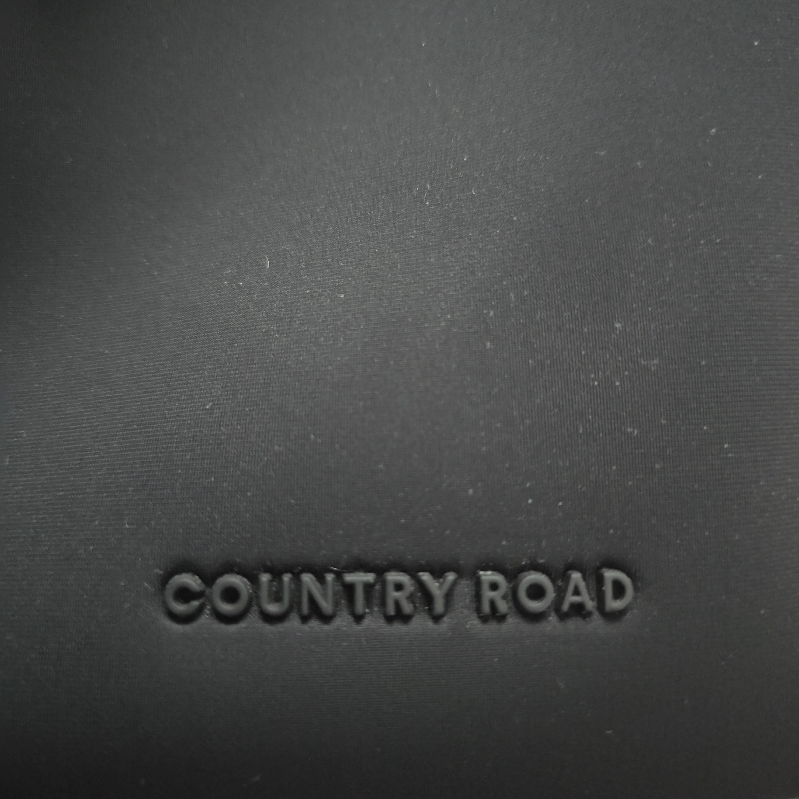 Text 'COUNTRY ROAD' embossed on a dark fabric surface