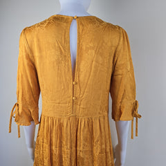 Mustard yellow dress with ruffled details on a mannequin against a light gray background