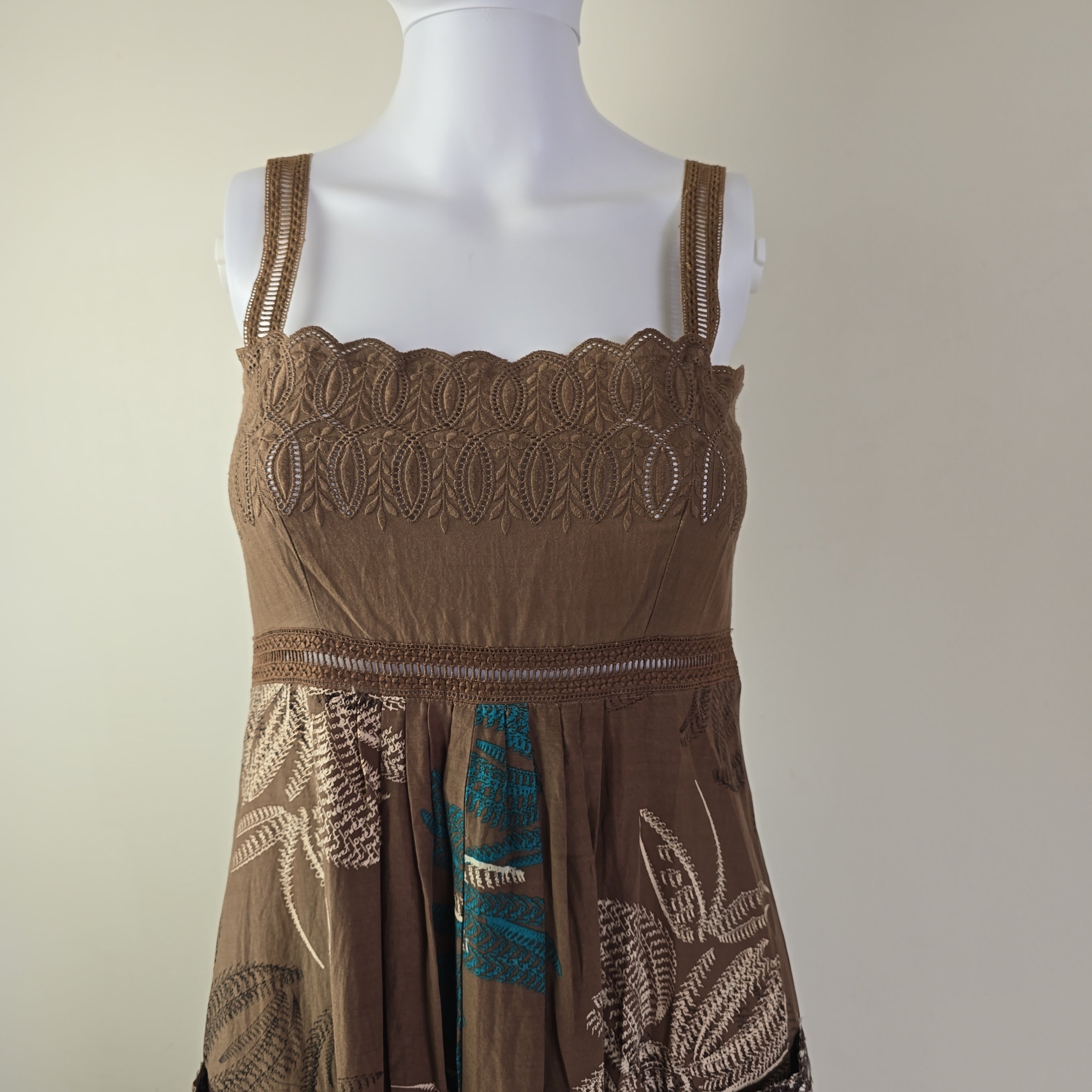 Brown dress with intricate lace and embroidery on a mannequin against a beige background