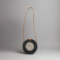 Black woven handbag with a brown strap on a tiled floor