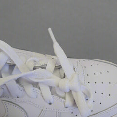 Close-up of a white sneaker with laces on a beige background