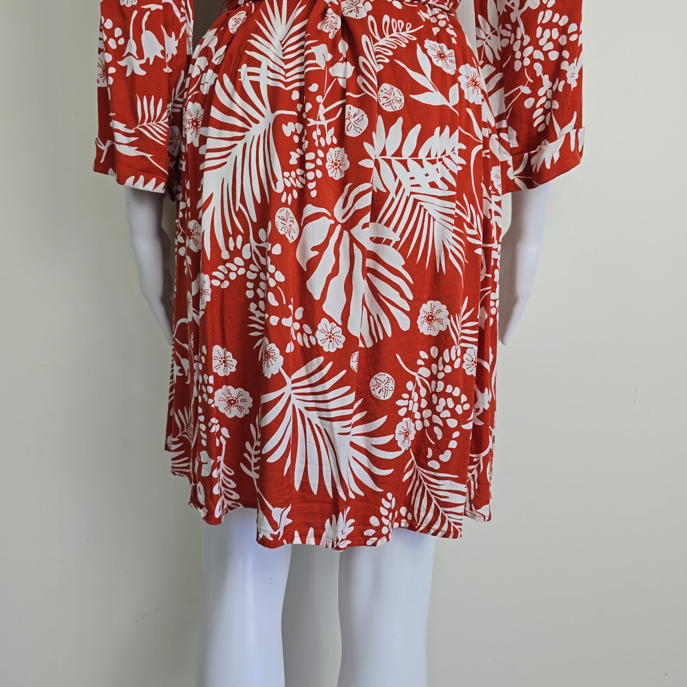 Red fabric with white floral and leaf pattern on a mannequin against a plain background