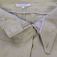 Close-up of beige pants with a visible brand tag, showing details like buttons and fabric texture.