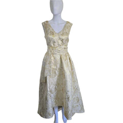 Eileen Kirby white and gold brocade dress with a high-low hemline and deep V-neckline on a mannequin against a neutral background.