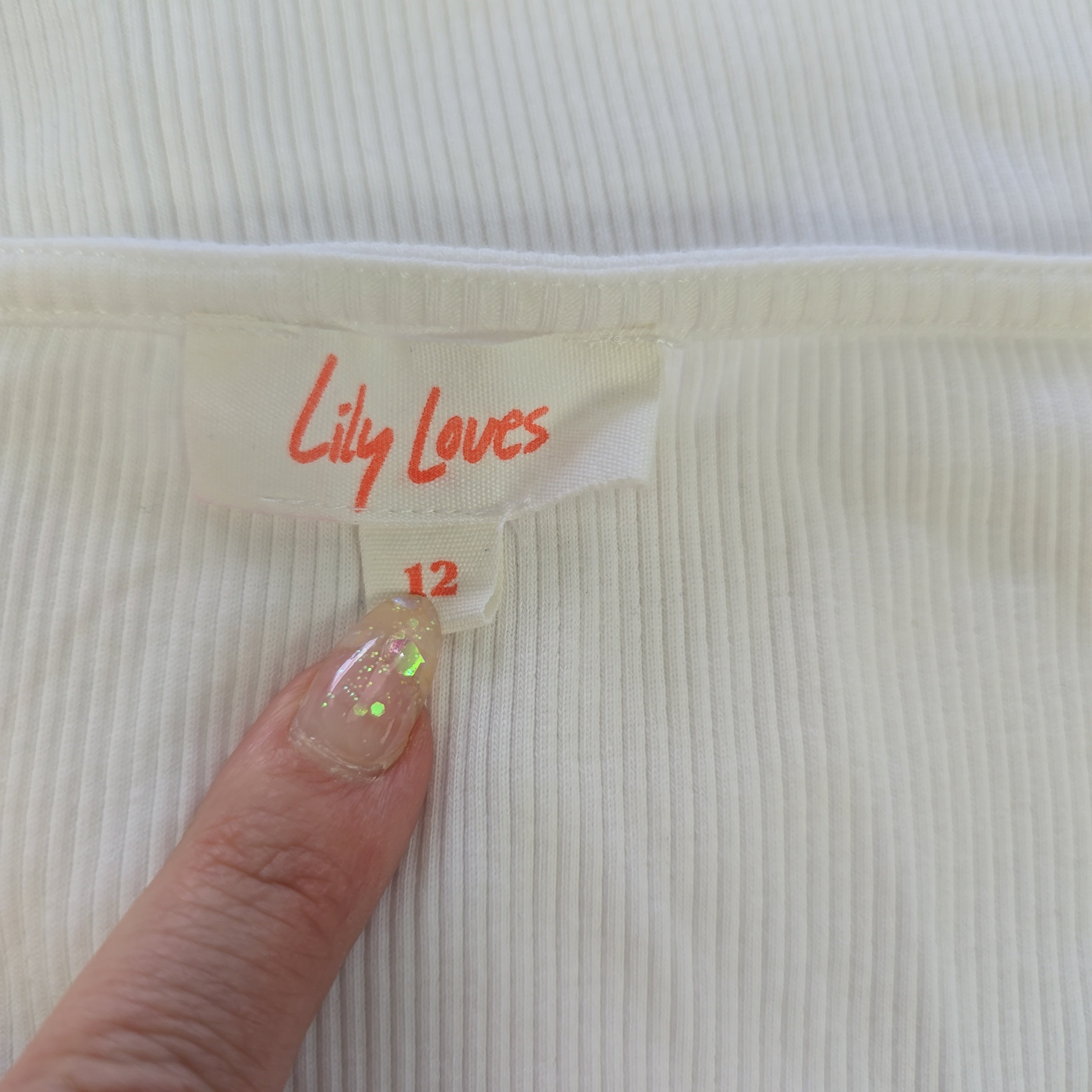 Hand holding a 'Lily Loves' product tag on a textured white background